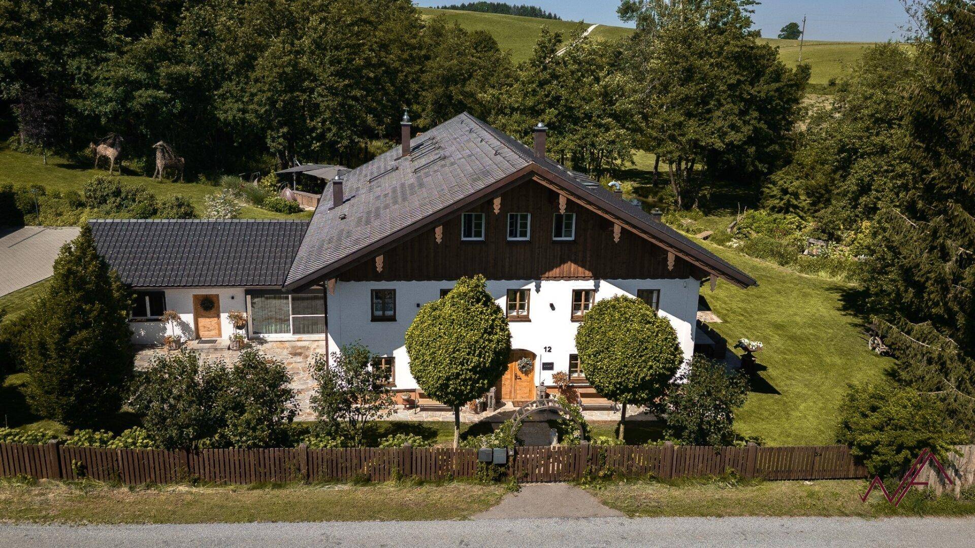 Traditionelles Landhaus mit gepflegtem Vorgarten, Holzzaun und zwei Bäumen vor dem Eingangsbereich.