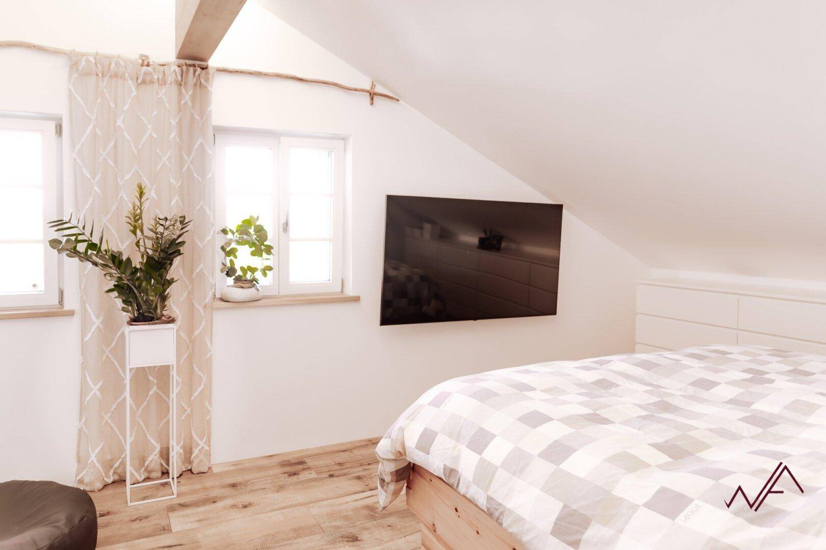 Gemütliches Schlafzimmer im Dachgeschoss mit Holzboden, schrägen Wänden und Fenster für Tageslicht.