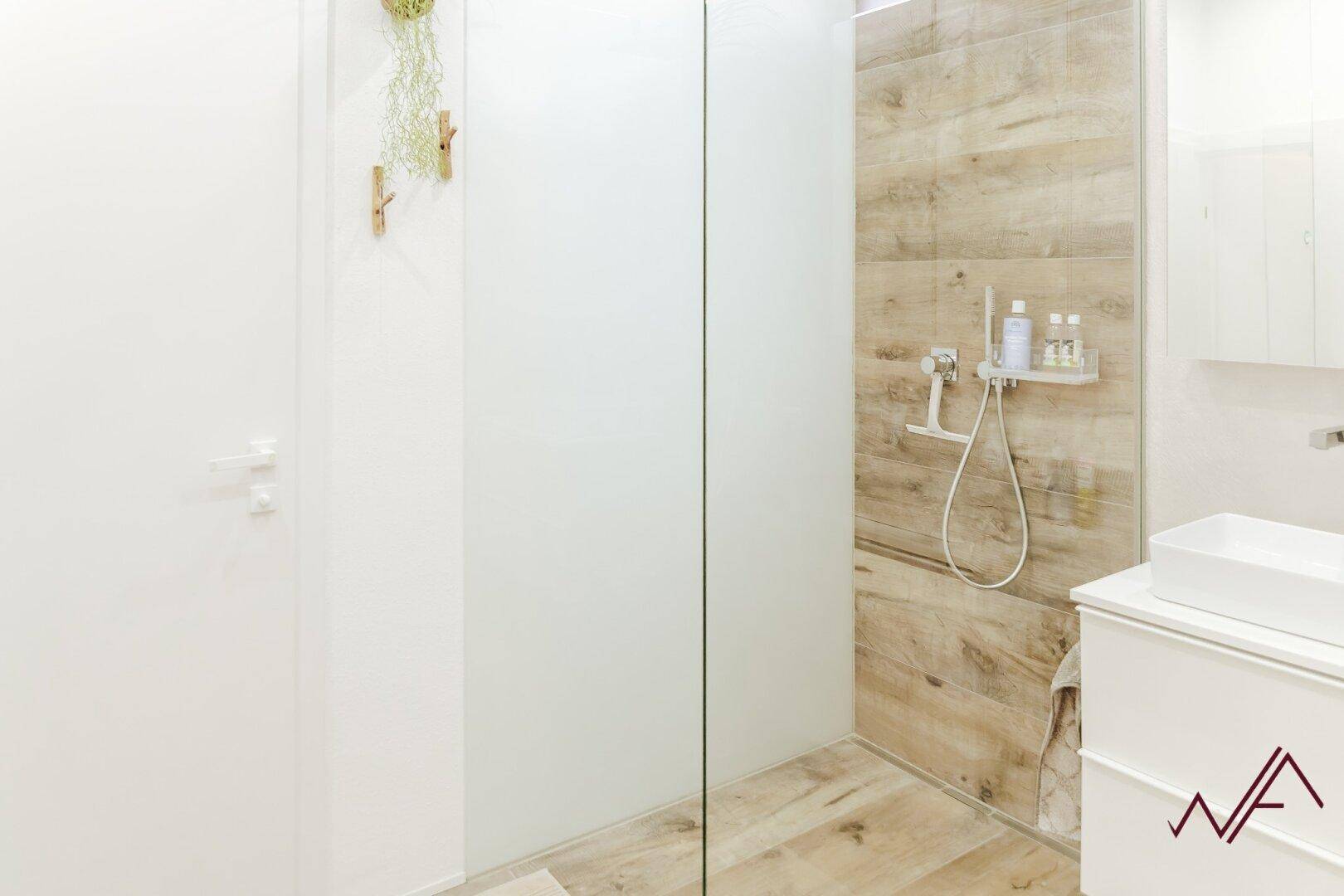 Helles Badezimmer mit moderner Dusche, weißen Wänden und Holzoptik-Fliesen.