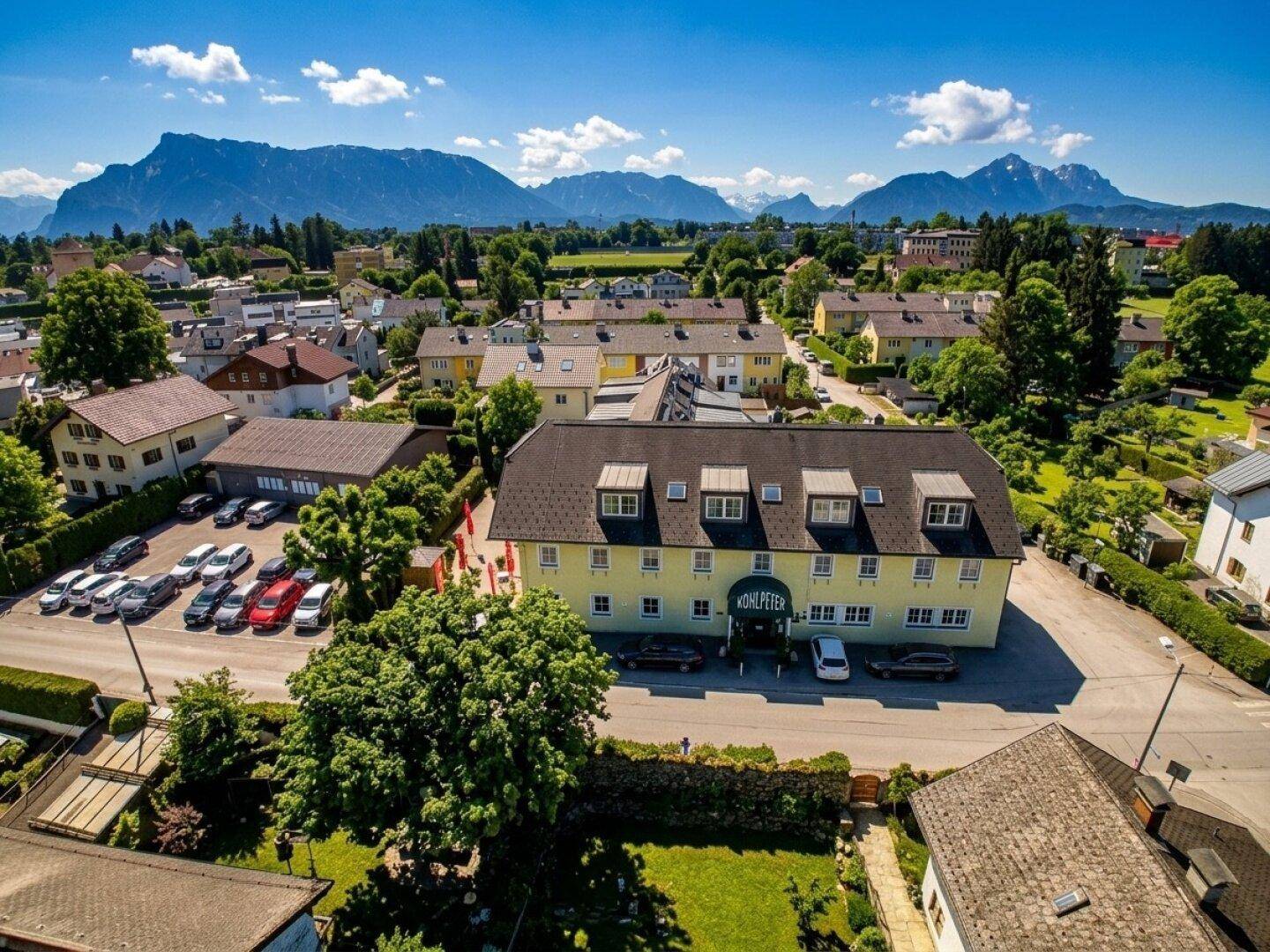 Luftaufnahme des Gebäudes in einer ländlichen Umgebung mit Bergen im Hintergrund und umliegenden Häusern.