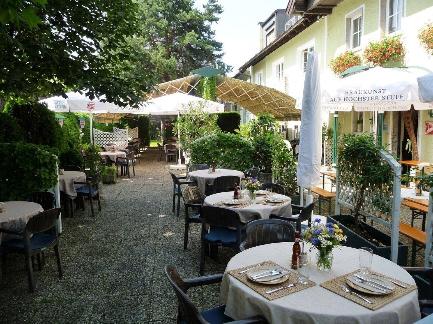 Gemütliche Außenterrasse mit vielen Tischen, Sonnenschirmen und üppiger Bepflanzung.