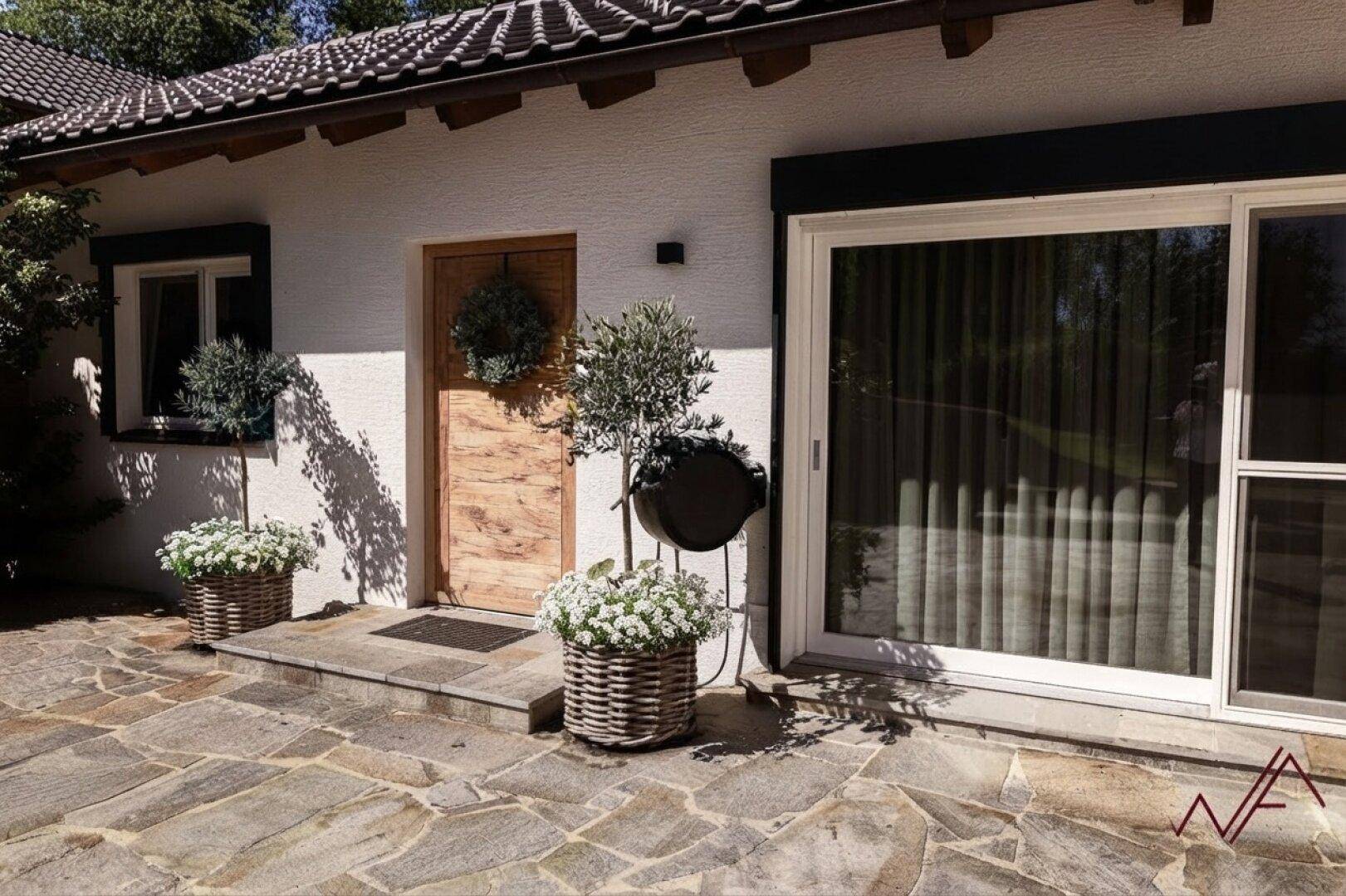 Eingangsbereich mit großer Glasschiebetür, Holztür und gepflastertem Vorplatz.