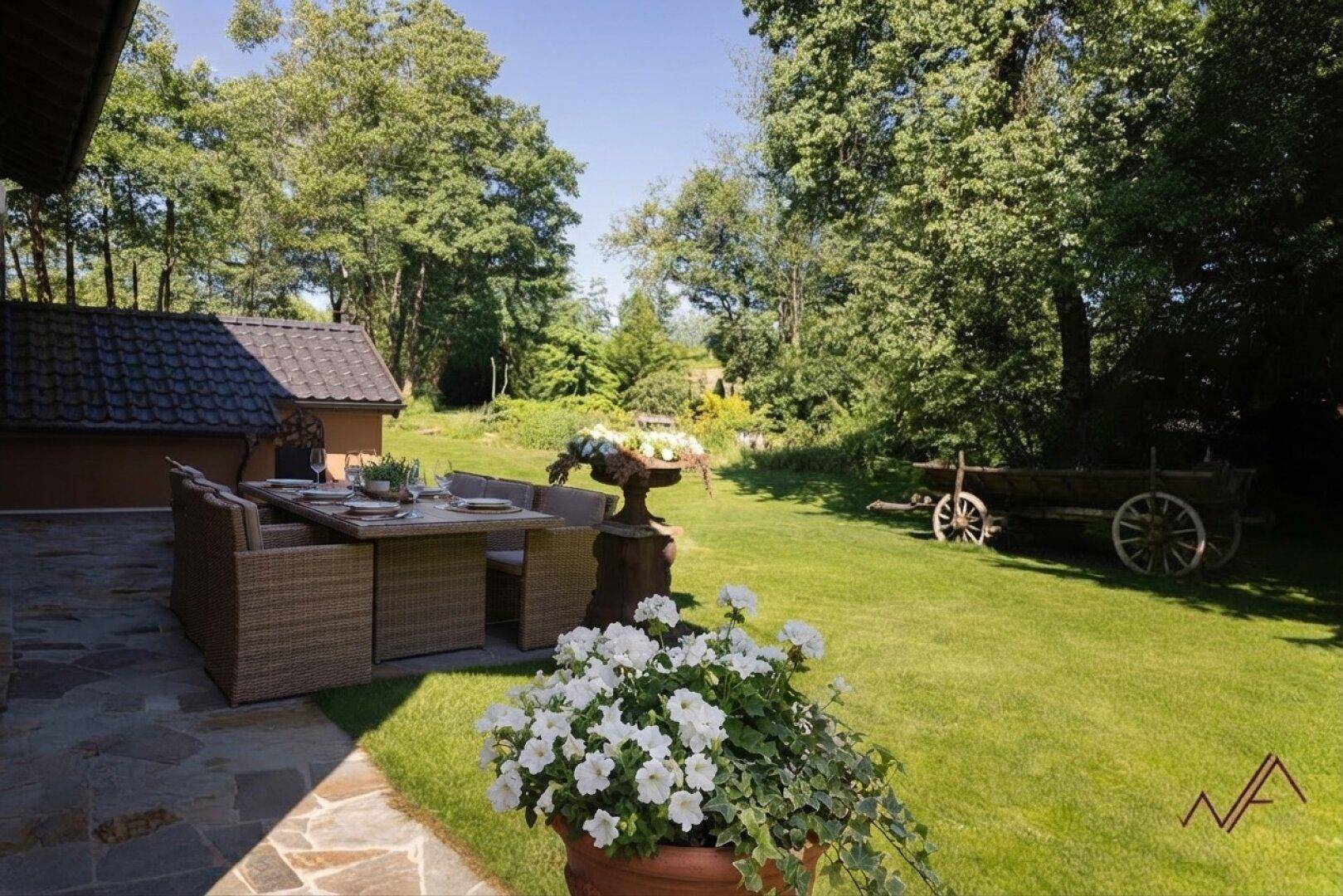 Großer Garten mit Essbereich im Freien, gepflegtem Rasen und dekorativem Holzwagen.