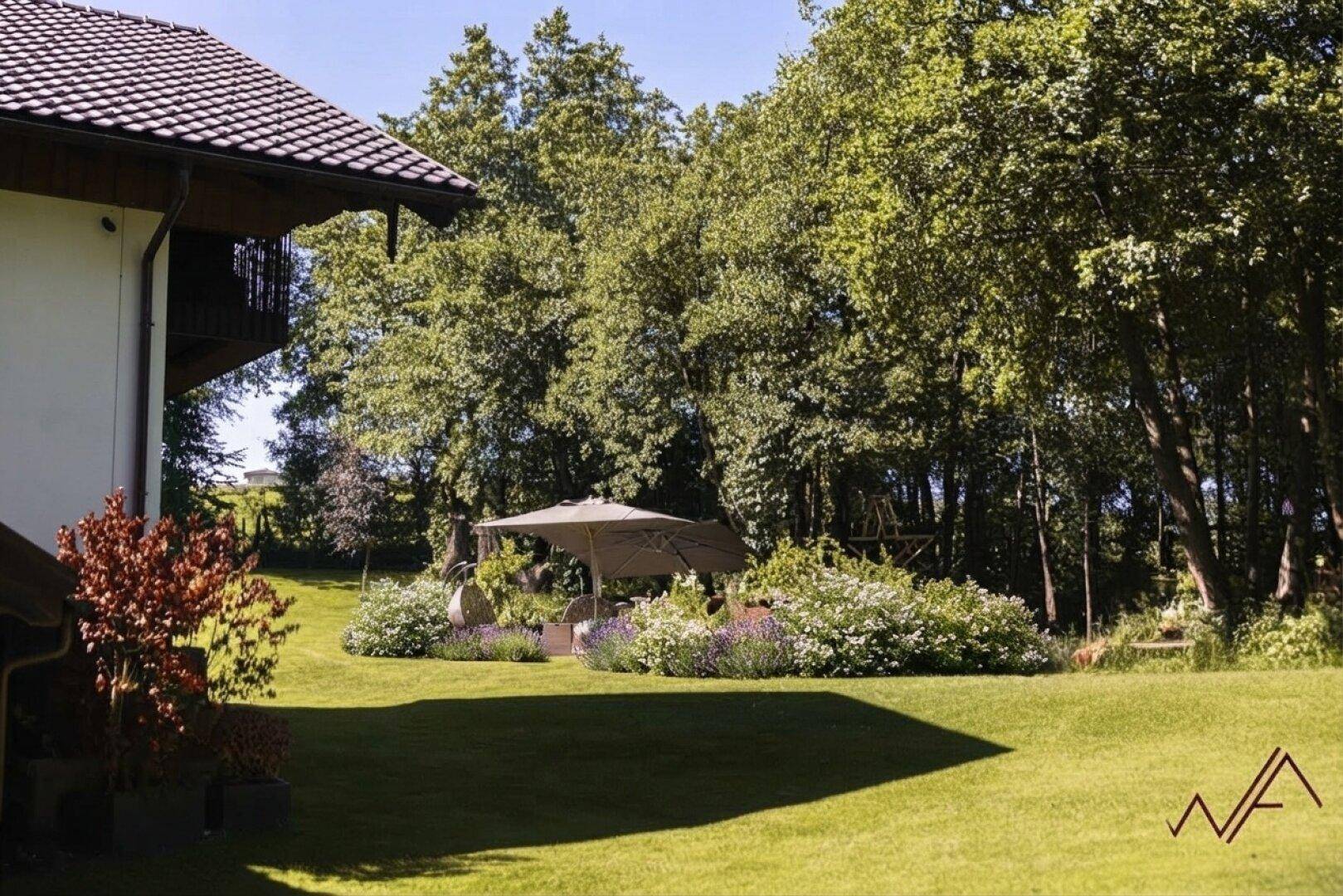 Großer gepflegter Garten mit Rasenfläche, altem Baumbestand und gemütlichem Sitzbereich unter einem Sonnenschirm.