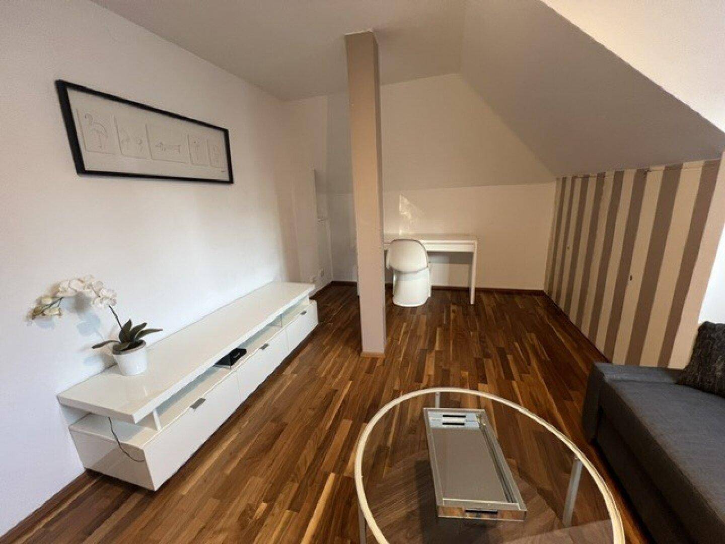 Wohnbereich im Dachgeschoss mit Holzboden, weißem Sideboard und einem praktischen Arbeitsplatz.