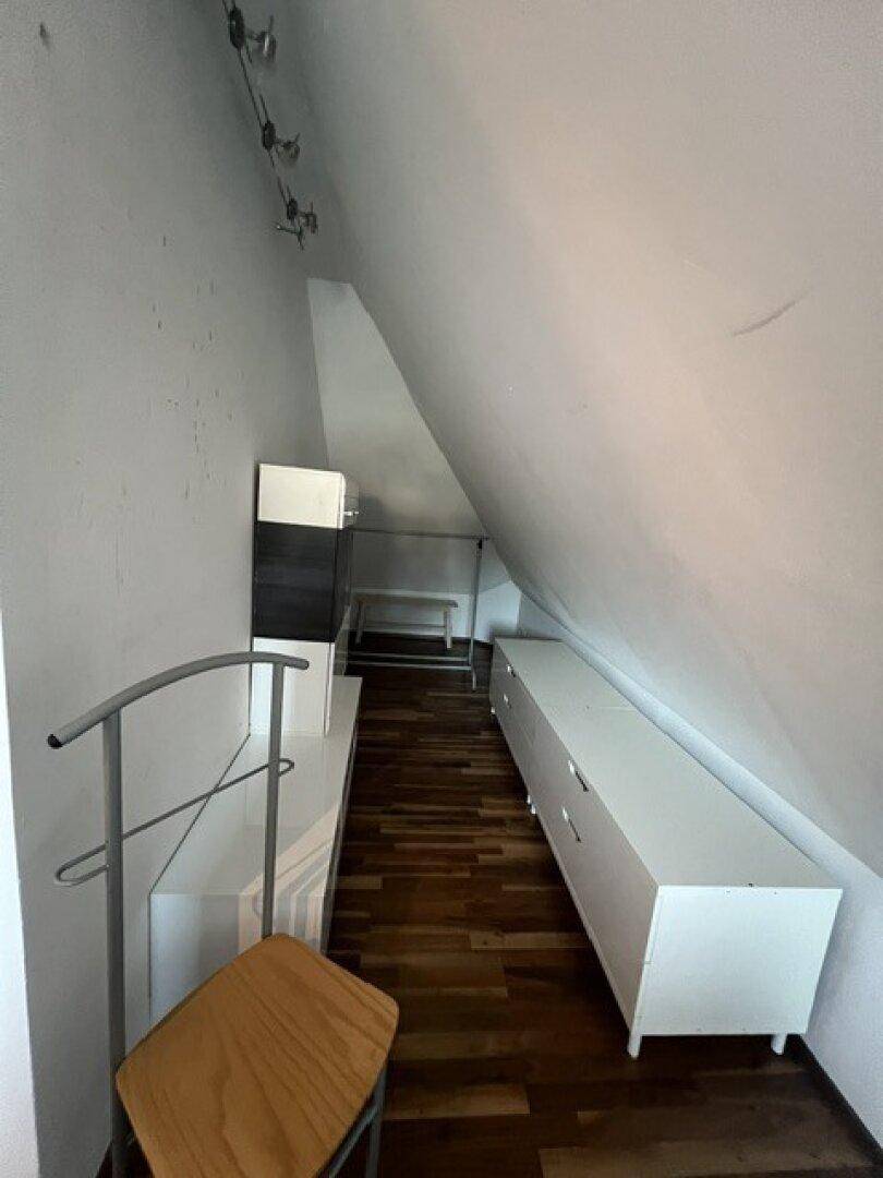 Schmaler Raum im Dachgeschoss mit Holzboden und praktischen Aufbewahrungsmöbeln unter der Schräge.