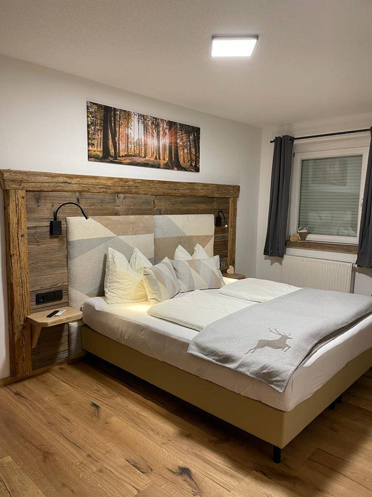 Helles Schlafzimmer mit Doppelbett, Holzkopfteil und einem großen Wandbild über dem Bett.
