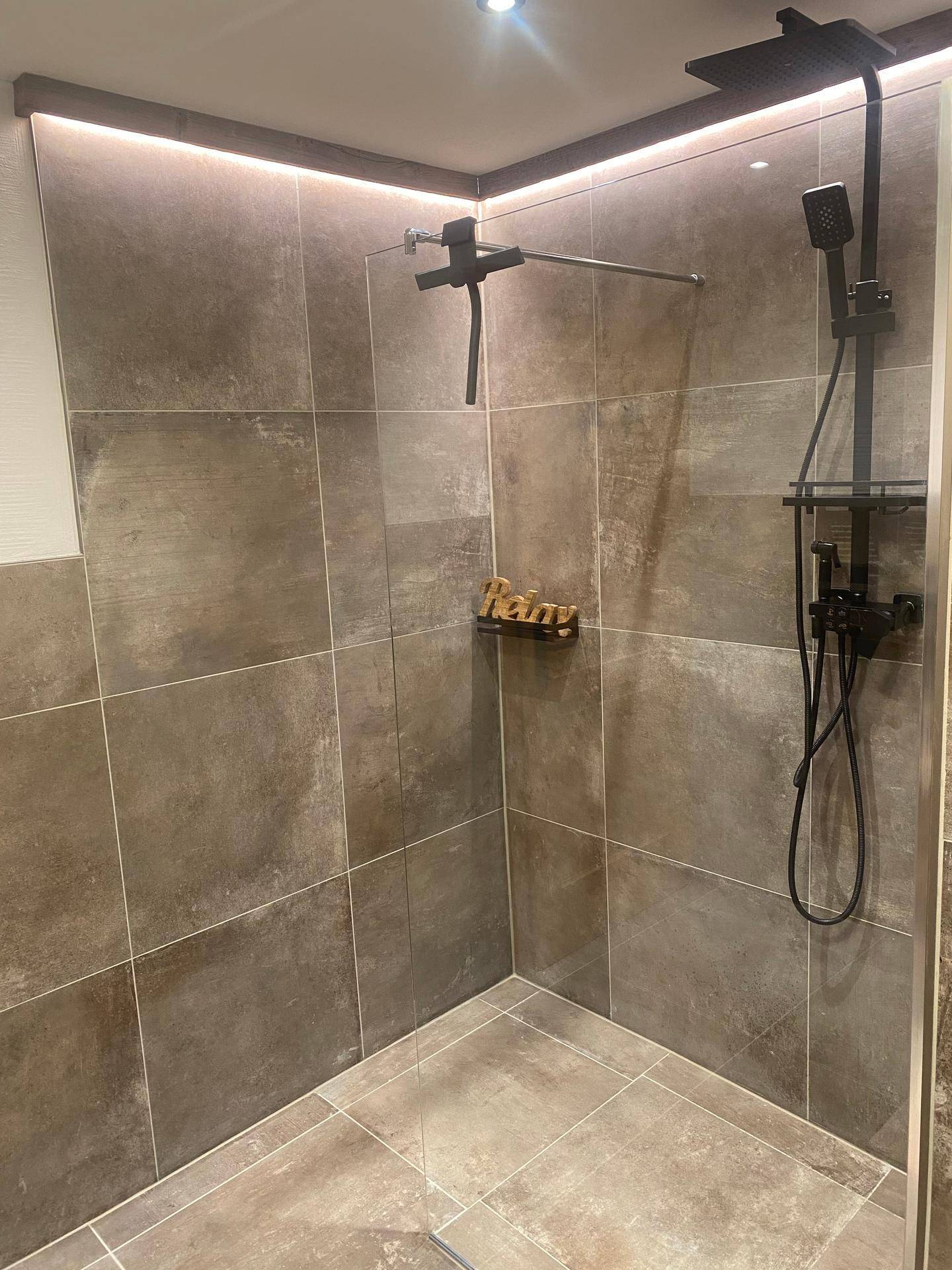 Moderne begehbare Dusche mit dunklen Fliesen und integrierter Beleuchtung für ein Spa-Gefühl.