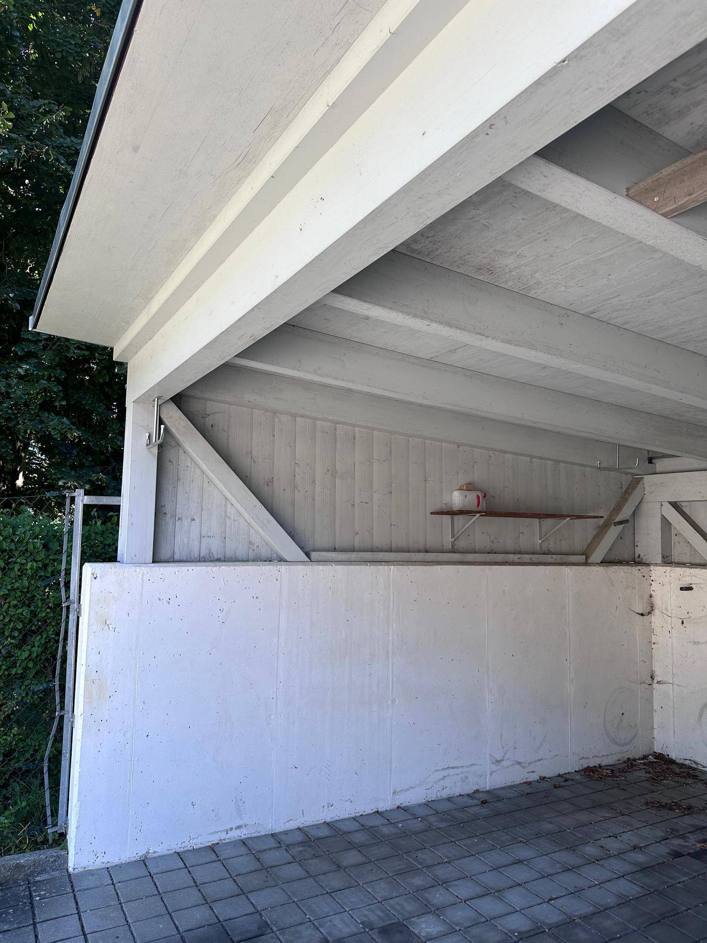 Überdachter Stellplatz oder Carport mit Betonboden und einfacher Holzkonstruktion.