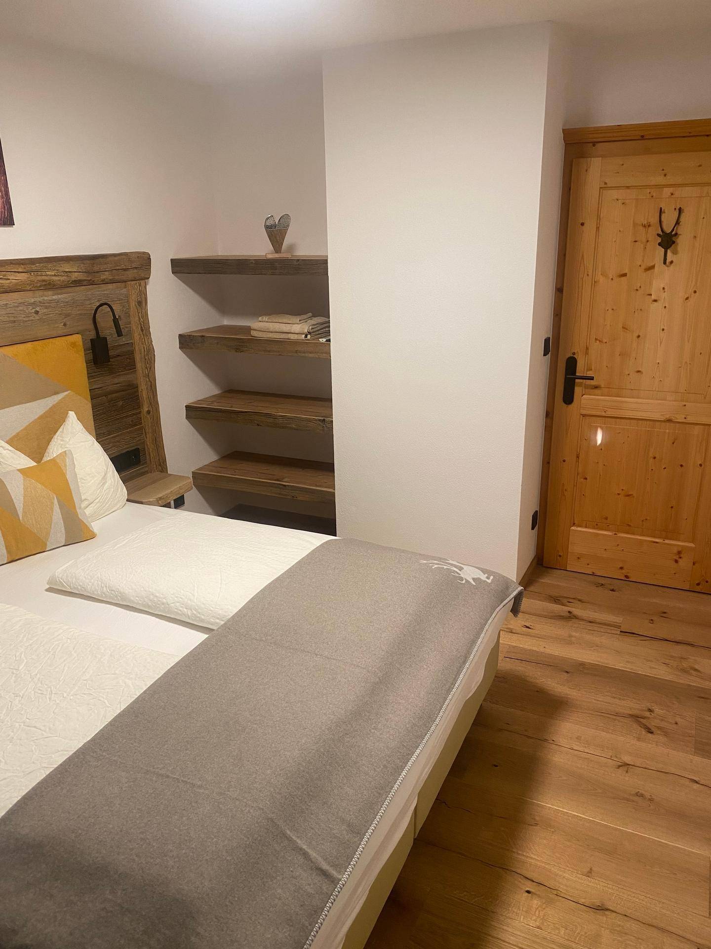 Schlafzimmer mit Holzboden, offenen Regalen und einer rustikalen Holztür im Landhausstil.