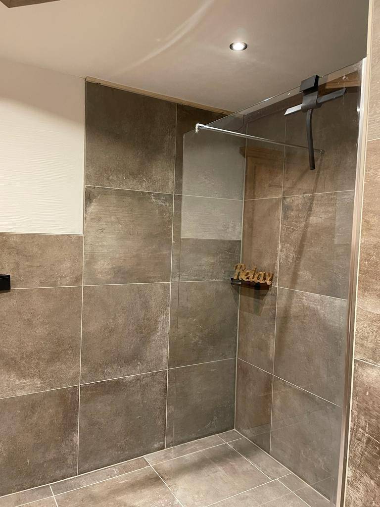 Moderne Duschkabine mit großformatigen Fliesen in Grautönen und Glasabtrennung.