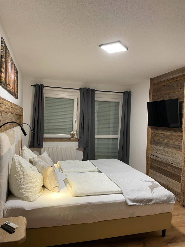 Gemütliches Schlafzimmer mit Holzbett, Fernseher und rustikaler Wandverkleidung aus Altholz.