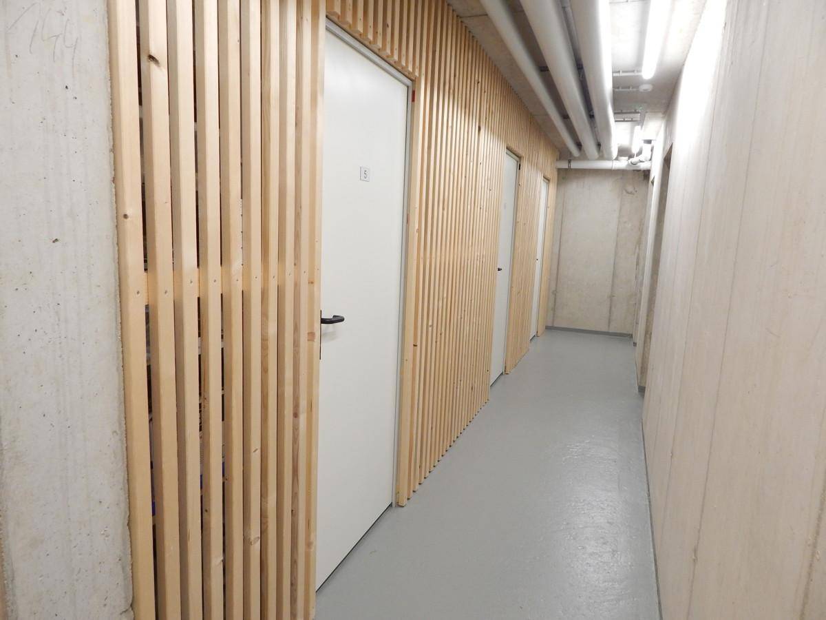 Kellerflur mit Sichtbetonwänden, Holzlamellenverkleidung und Türen zu den Abstellräumen.