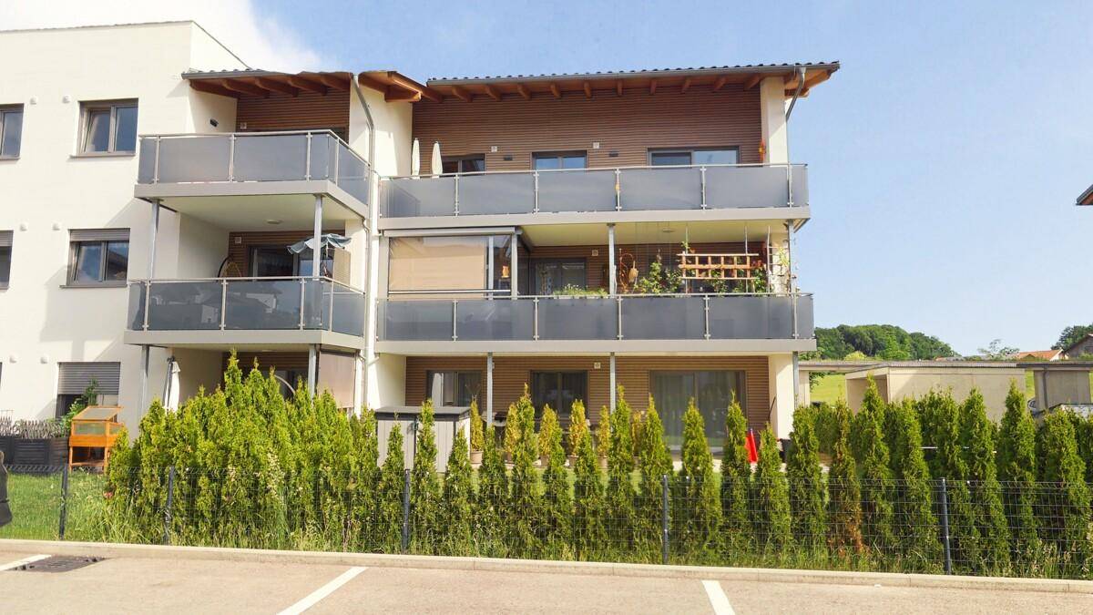 Moderne Wohnanlage mit mehreren Balkonen und einer gepflegten Hecke im Außenbereich.