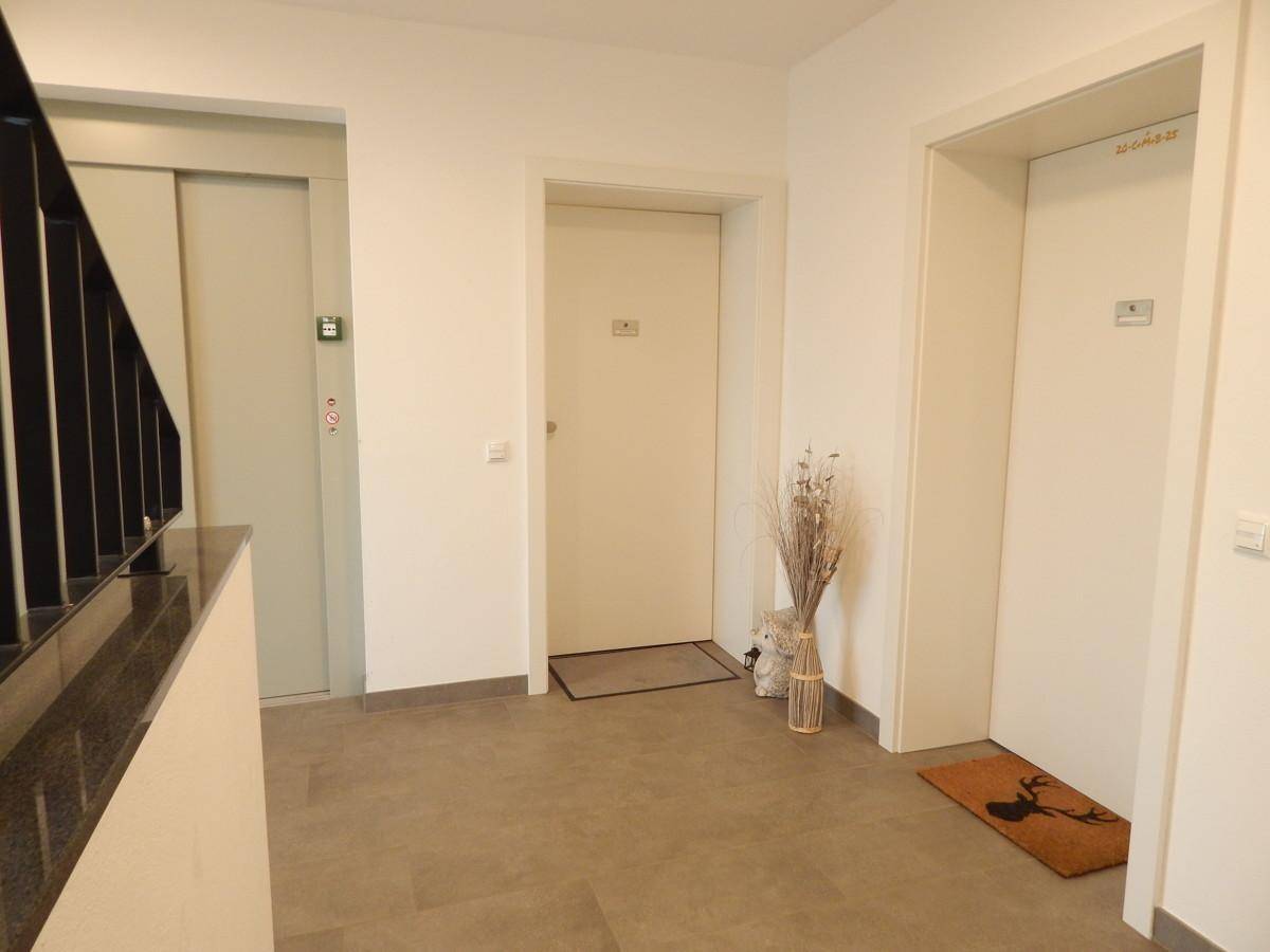 Heller Eingangsbereich mit zwei Wohnungstüren, Fliesenboden und Zugang zu einem modernen Aufzug.