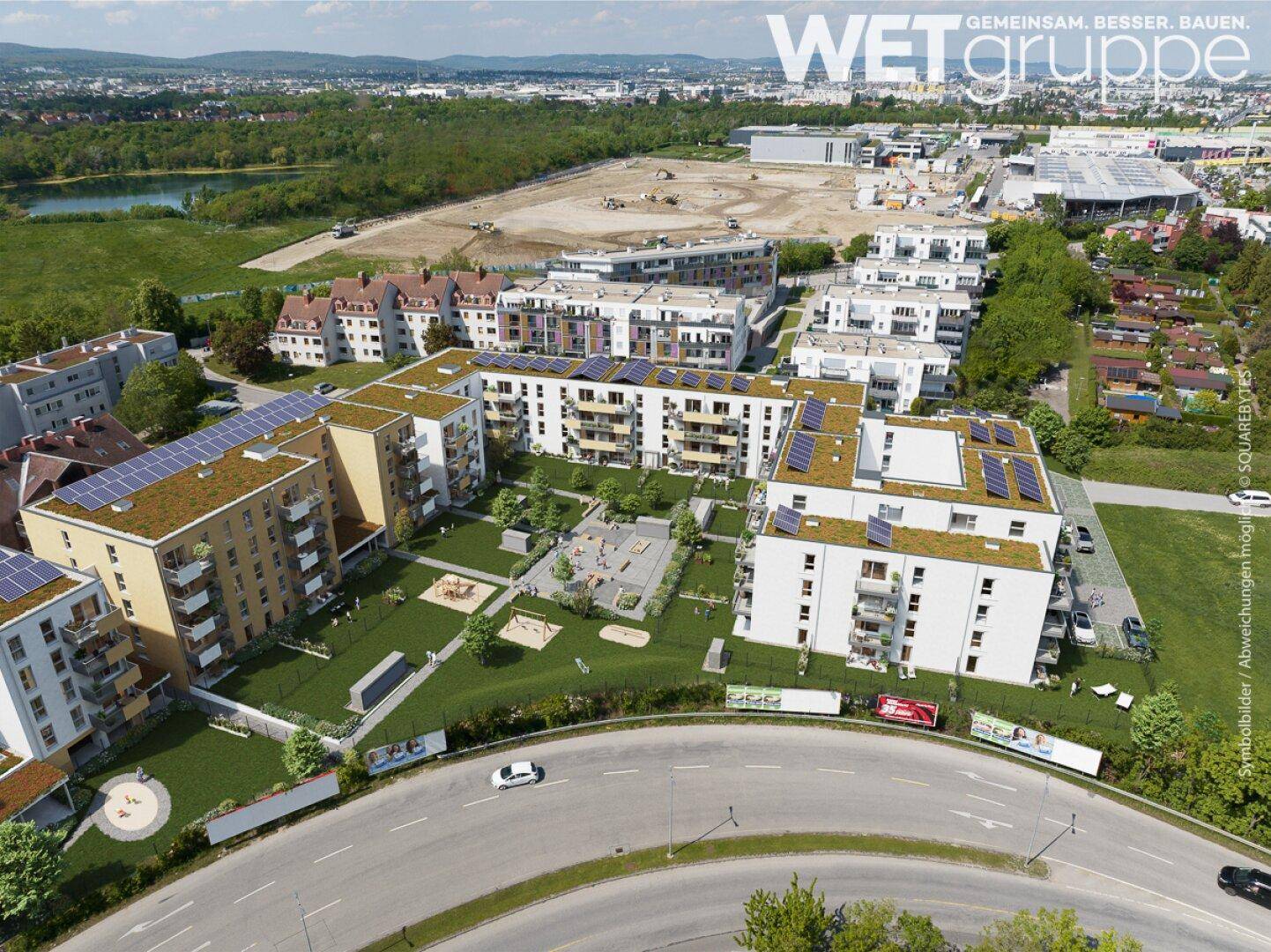 Weitläufige Luftaufnahme eines modernen Wohnkomplexes mit Gründächern und Solaranlagen in städtischer Umgebung.