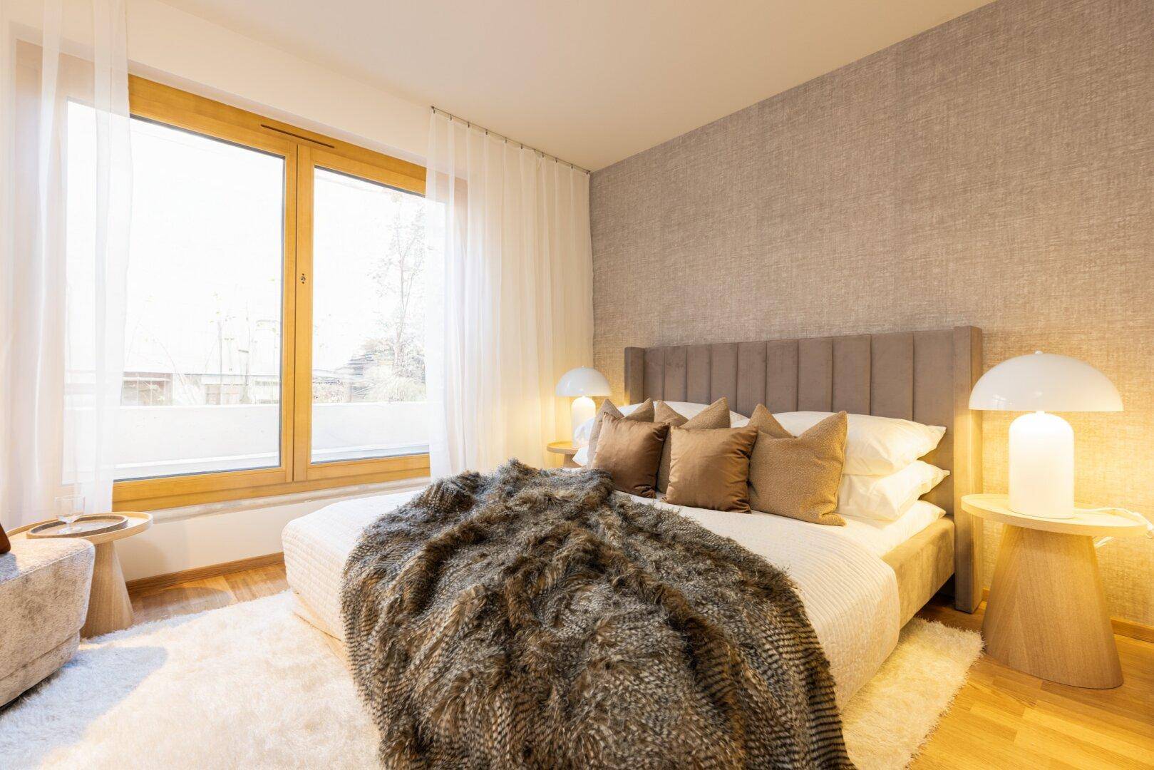 Gemütliches Schlafzimmer mit großem Bett, Nachttischen und einem großen Fenster mit Vorhängen.