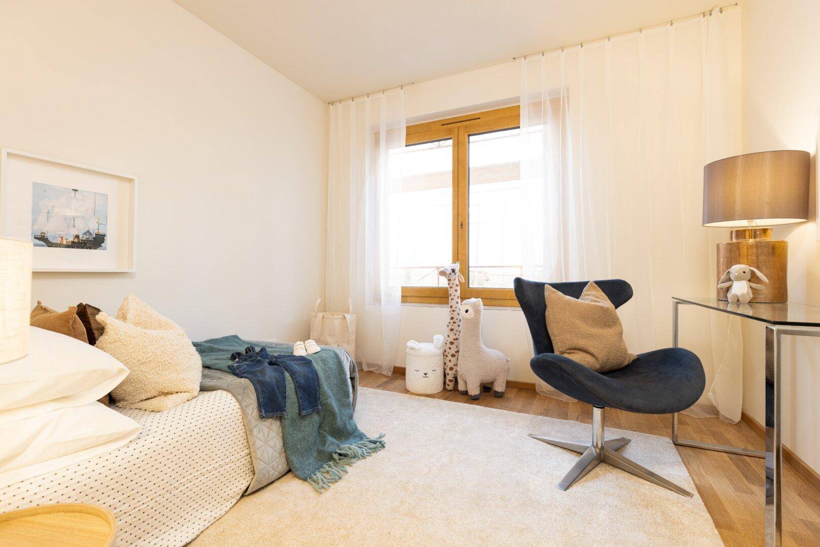 Helles Kinder- oder Gästezimmer mit Einzelbett, Schreibtisch und einem großen Fenster.
