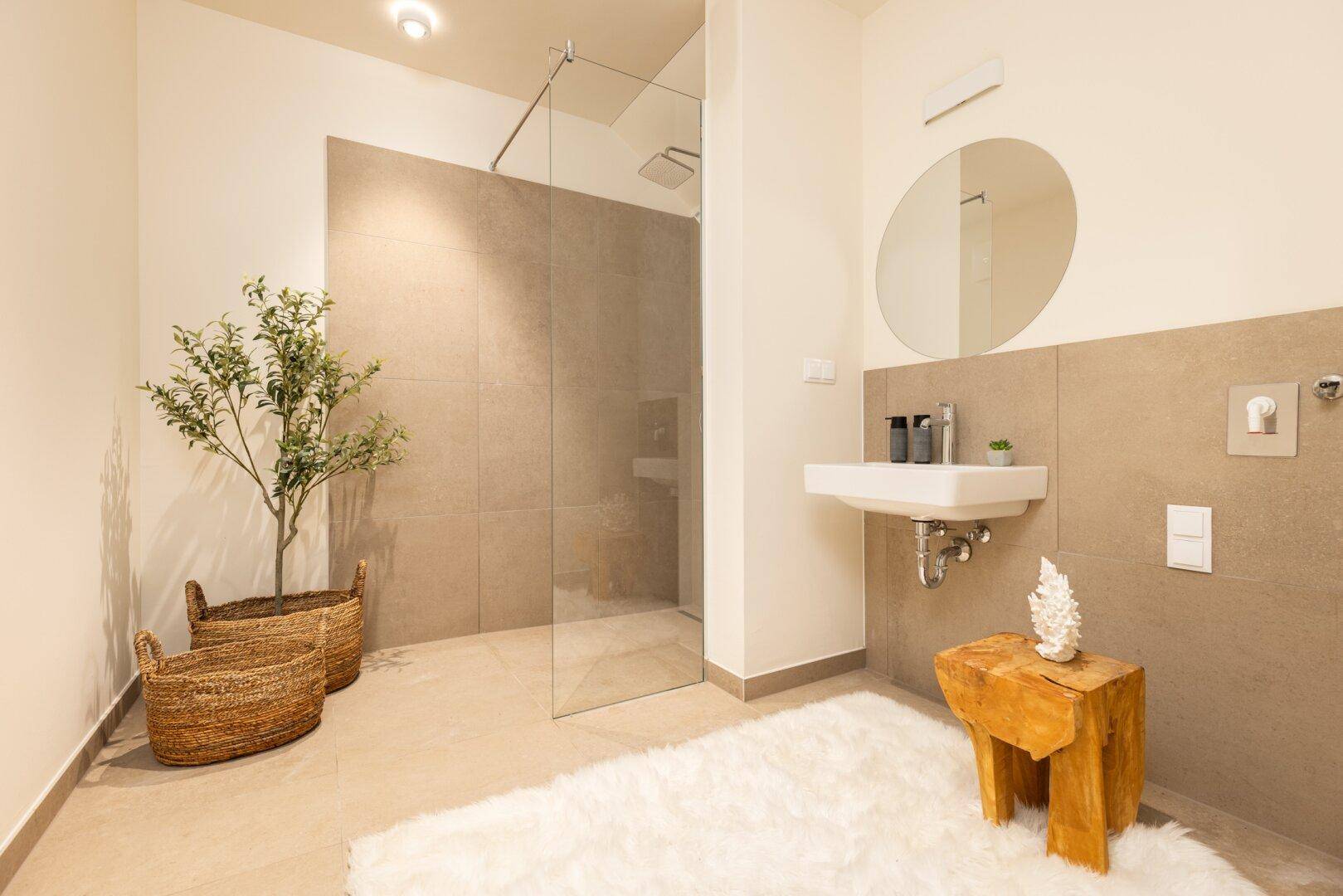 Modernes Badezimmer mit begehbarer Dusche, Einzelwaschbecken und runden Spiegel.
