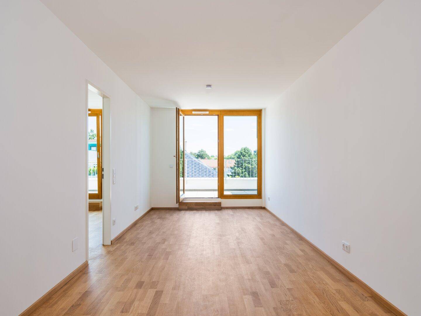 Geräumiger, heller Wohnraum mit Parkettboden und Zugang zum Balkon.