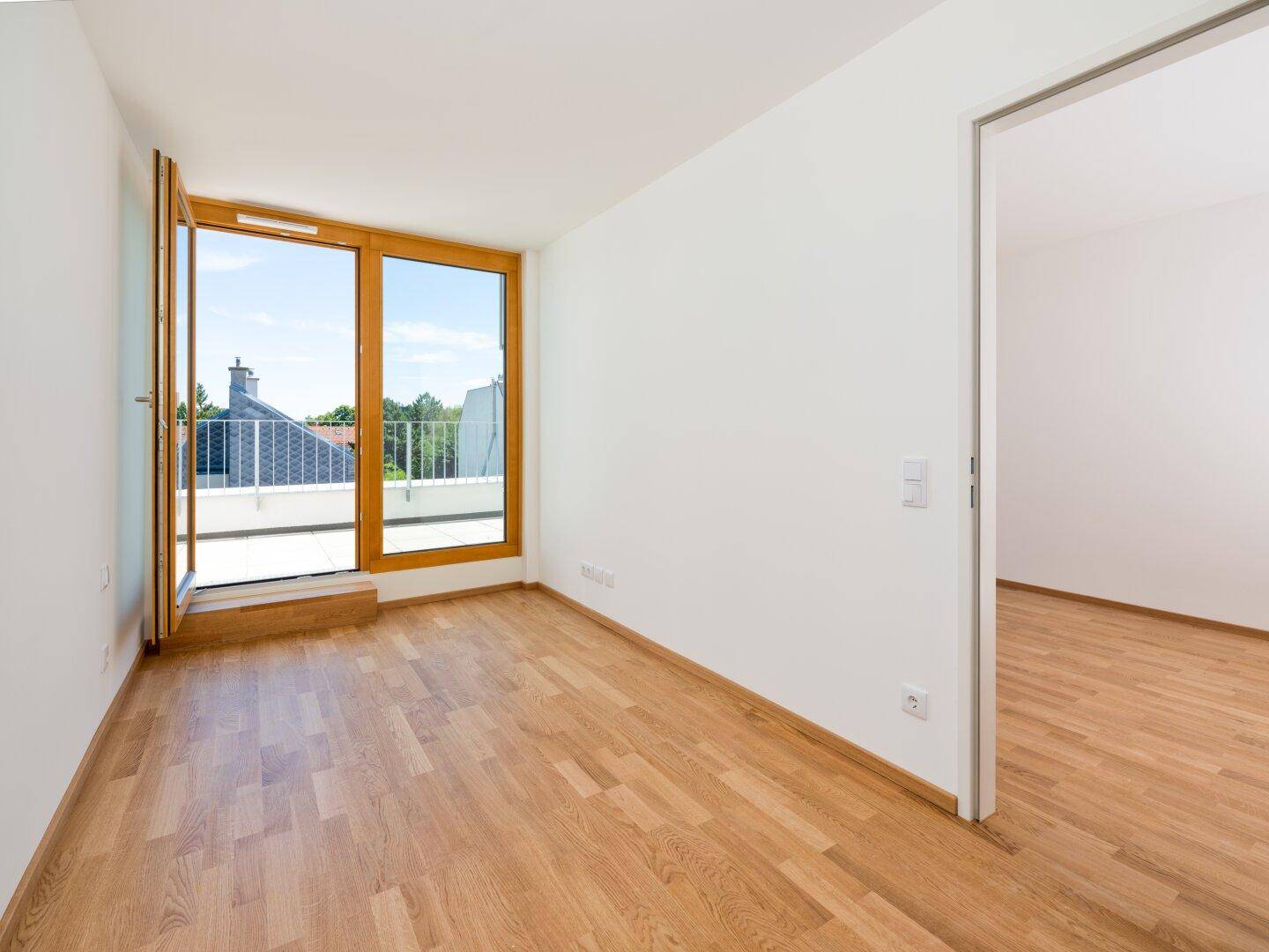 Heller Raum mit Holzboden und großen Fenstern, ideal als Schlaf- oder Wohnzimmer.