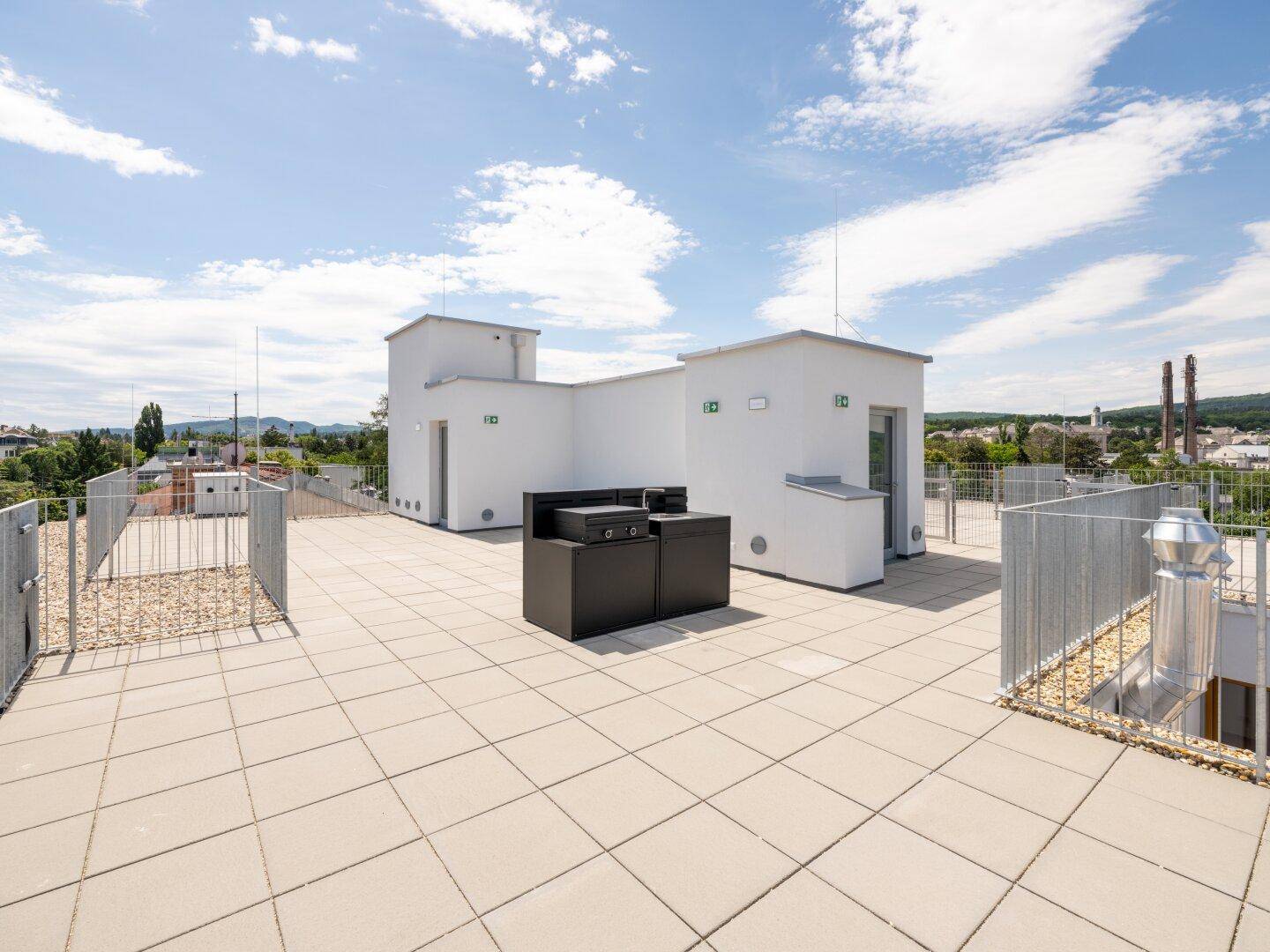 Geräumige Dachterrasse mit Fliesenboden und moderner Outdoor-Küche unter blauem Himmel.