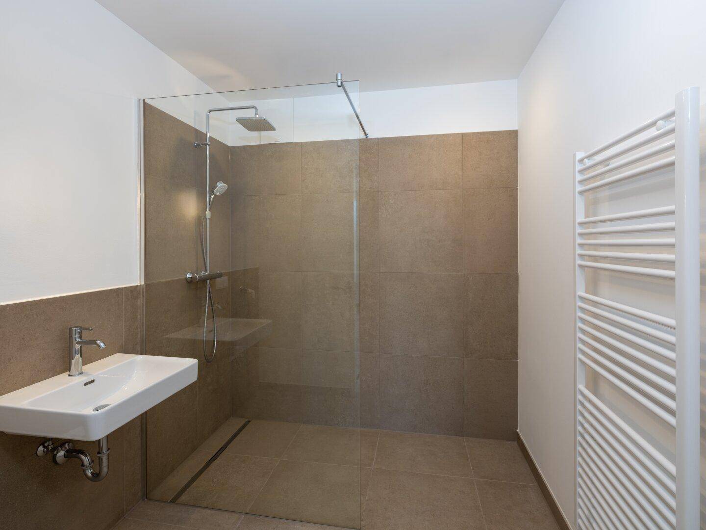 Modernes Badezimmer mit ebenerdiger Dusche, einzelnen Waschbecken und Handtuchheizkörper.