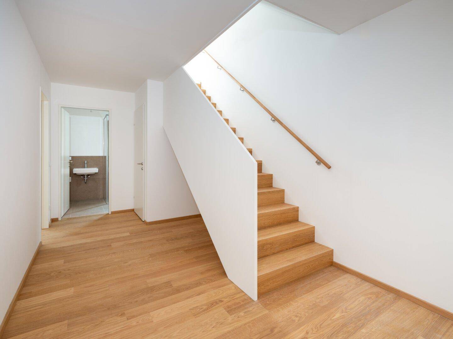 Heller Flur mit Holztreppe und Zugang zu einem Badezimmer, ausgestattet mit modernem Holzboden.