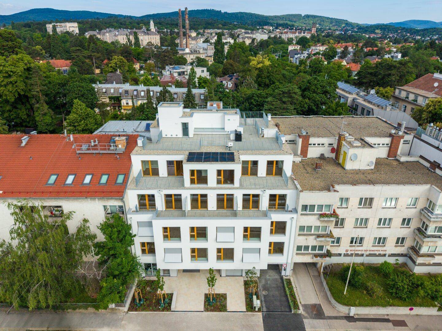 Moderne Wohnanlage mit weißer Fassade, großen Fenstern und Photovoltaikanlage auf dem Dach.
