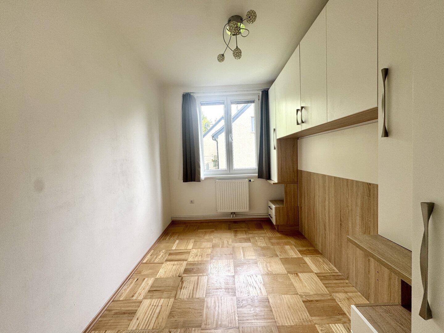Schlafzimmer mit Parkettboden, Einbauschränken und Fenster mit Blick auf die Umgebung.