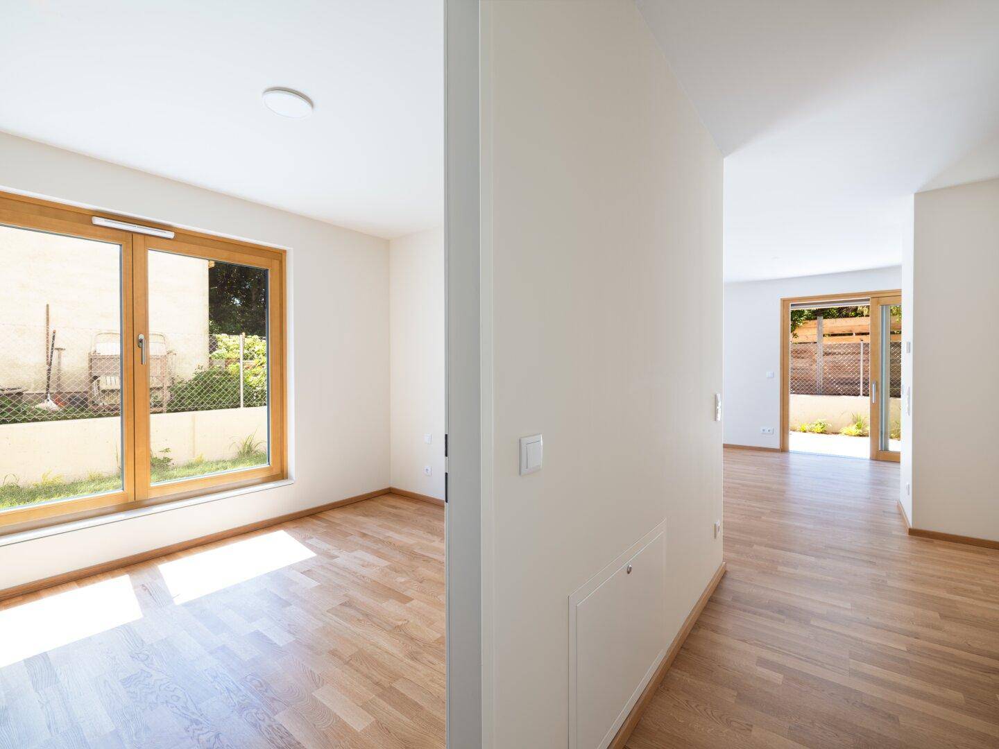 Heller Raum mit Holzboden und Fenster, der zu einem weiteren Bereich des Hauses führt.