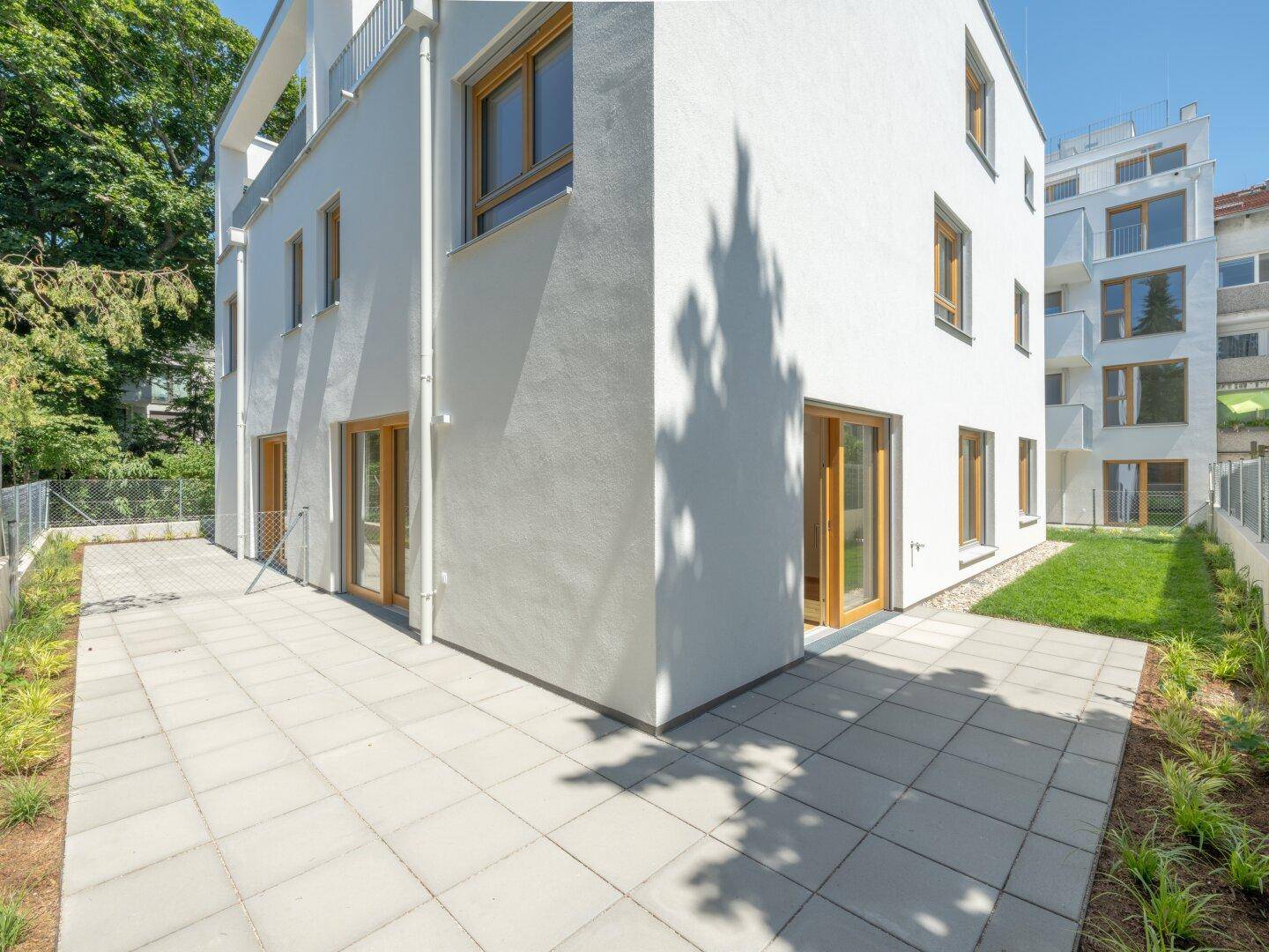 Moderne weiße Gebäudefassade mit großen Fenstern, Terrasse und kleinem Rasenbereich.