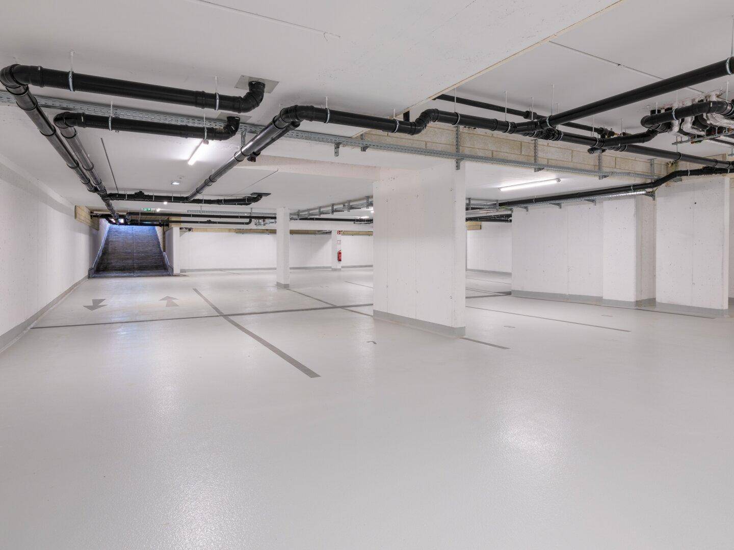 Geräumige Tiefgarage mit Betonboden und sichtbaren Installationen an der Decke.