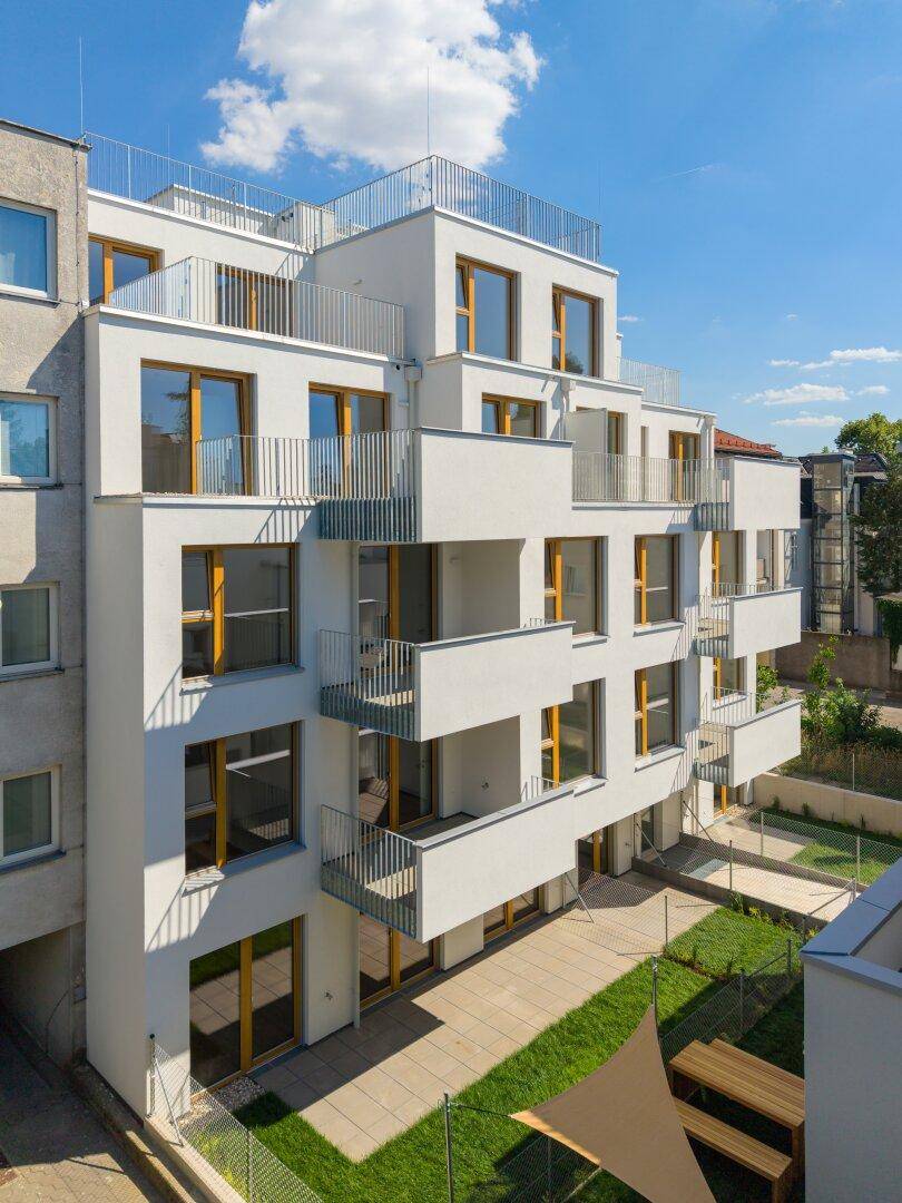 Moderne Gebäudefassade mit Balkonen, Terrassen und einem kleinen Gartenbereich im Erdgeschoss.