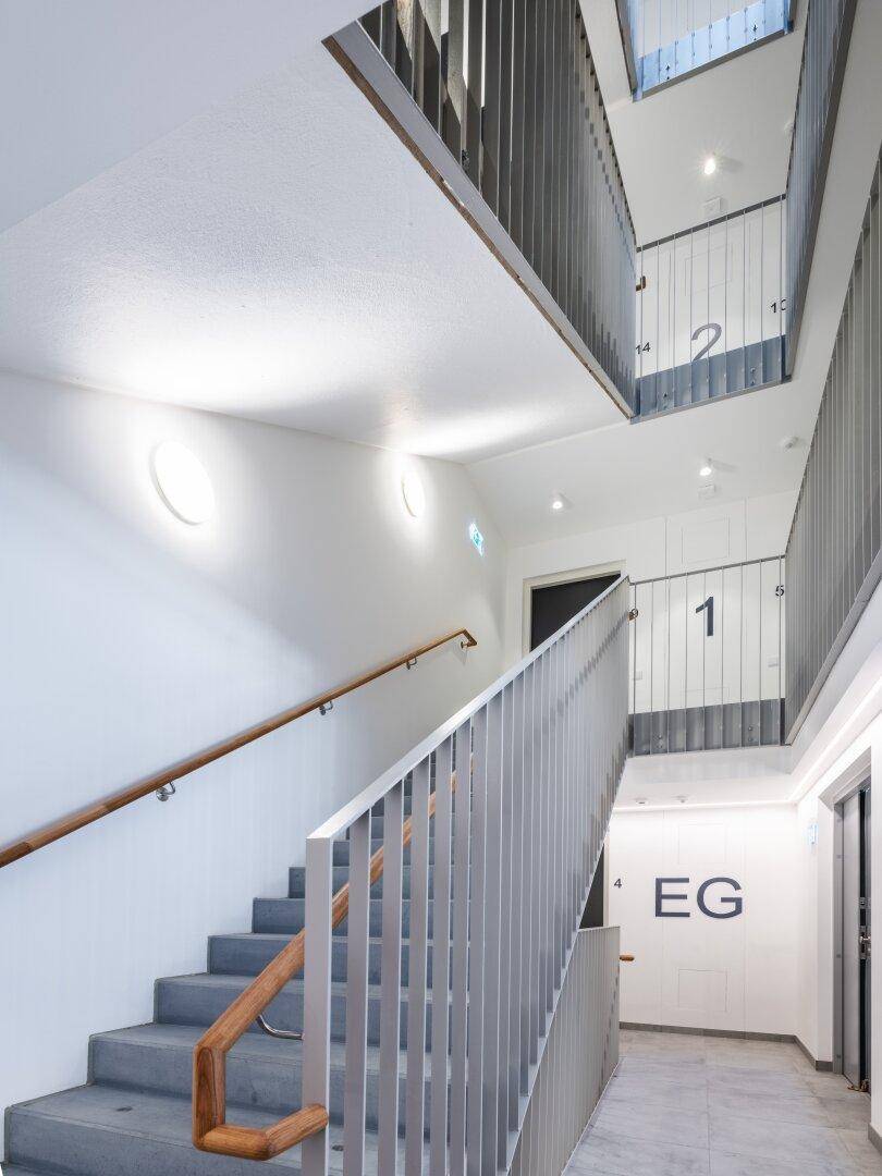 Modernes Treppenhaus mit Metallgeländer, Holzhandlauf und heller Beleuchtung.