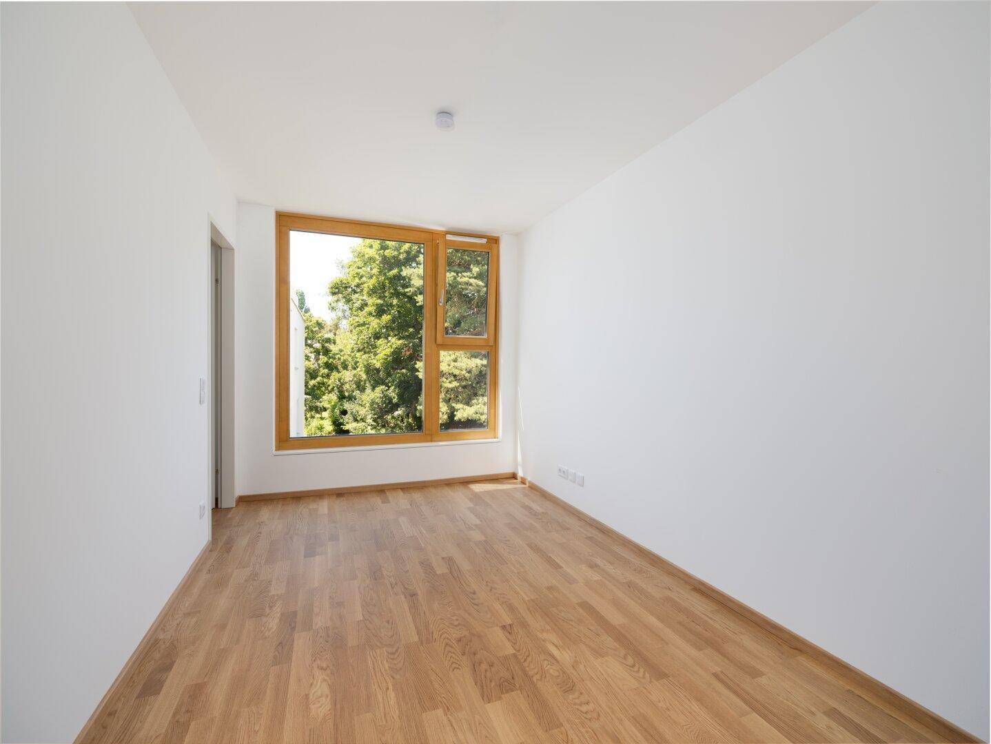 Helles Schlafzimmer mit Parkettboden und großem Fenster, das einen schönen Blick ins Grüne bietet.