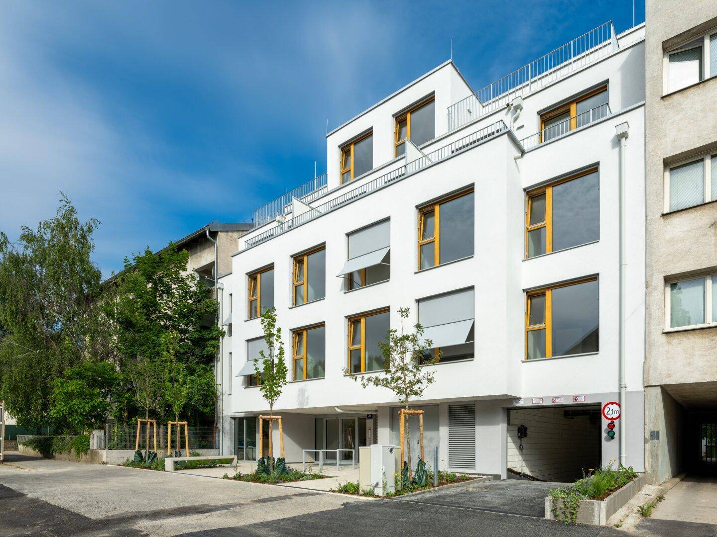 Moderne Gebäudefassade mit großen Fenstern und Zufahrt zur Tiefgarage.