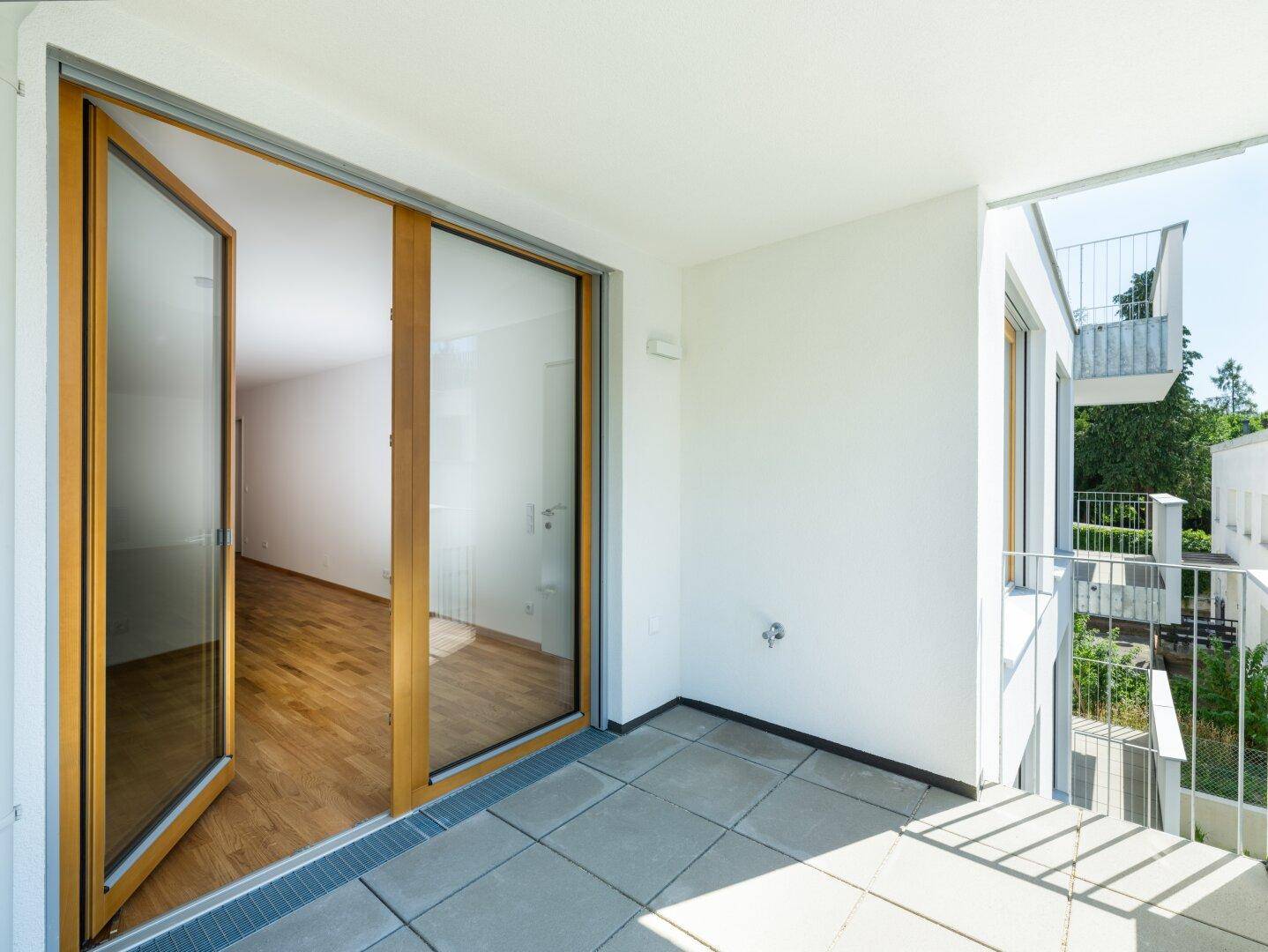 Heller Balkon mit Fliesenboden und Blick in einen leeren Innenraum.