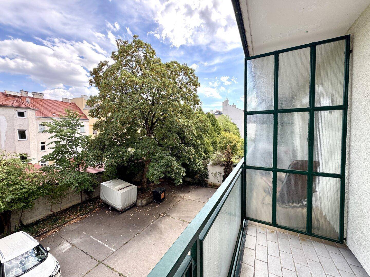 Balkon mit Fliesenboden und Blick auf den begrünten Innenhof mit alten Bäumen.
