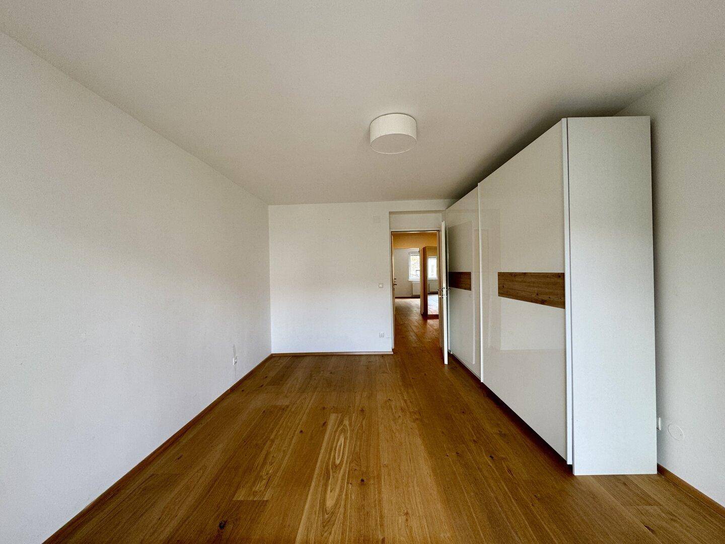 Schlafzimmer mit Holzboden, weißen Wänden und einem modernen Kleiderschrank.
