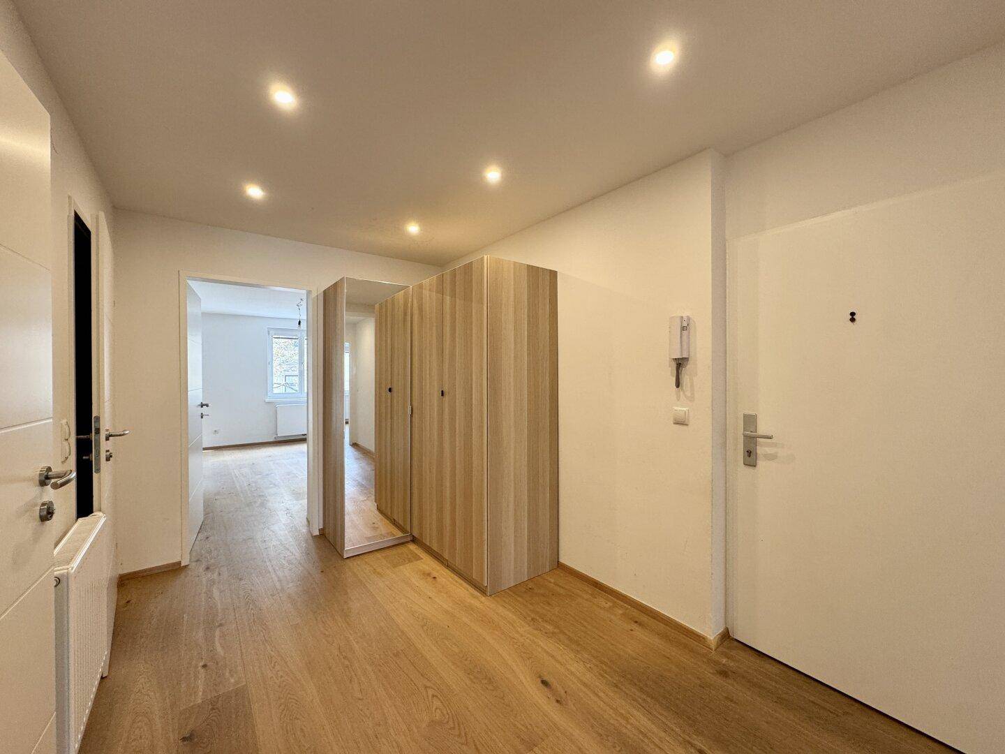 Heller Flur mit Holzboden, Einbauschränken und moderner Deckenbeleuchtung.