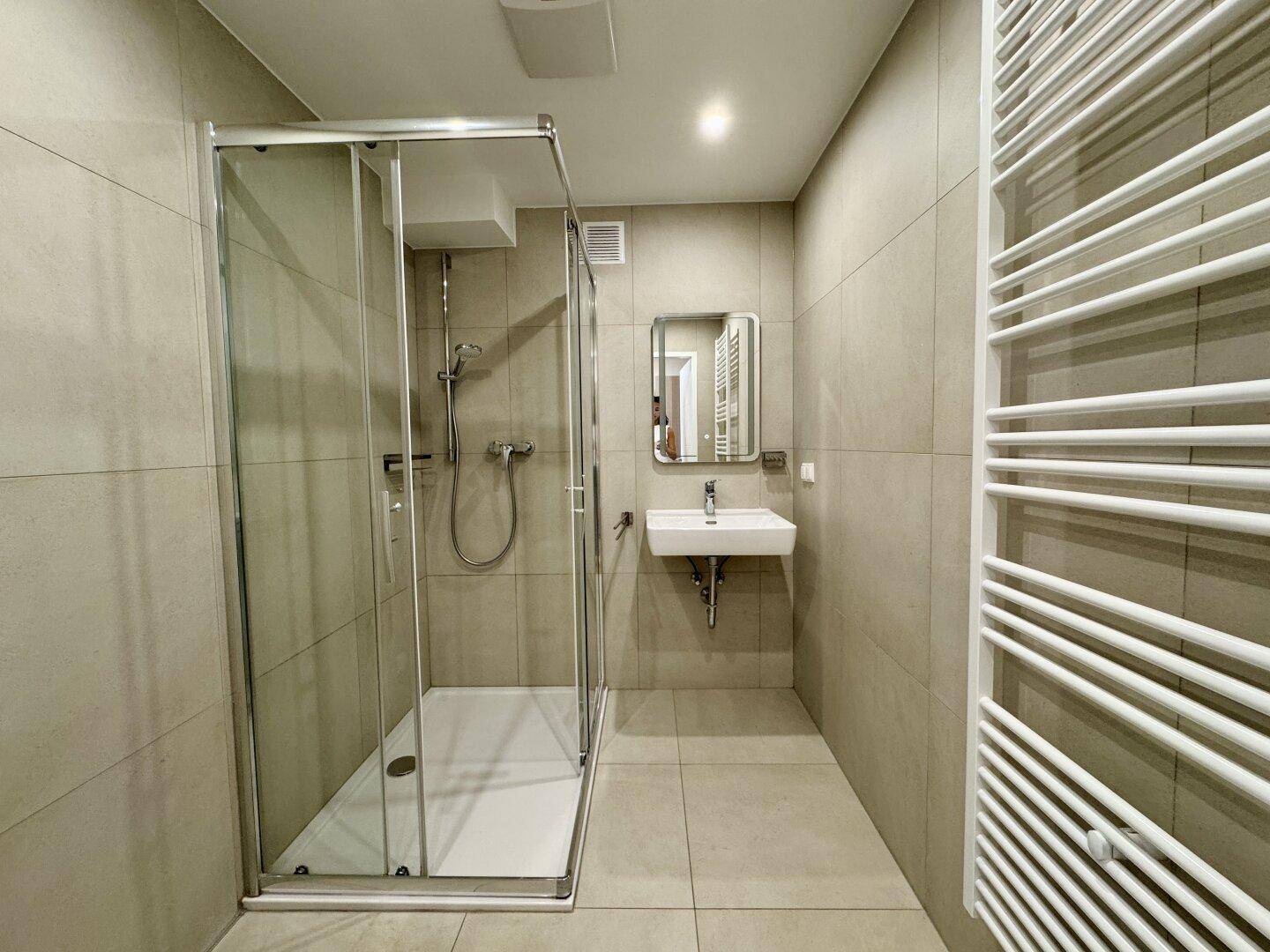 Modernes Badezimmer mit beigefarbenen Fliesen, Duschkabine und beheiztem Handtuchhalter.