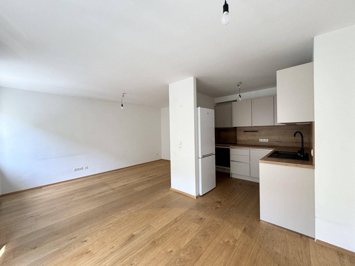 Moderner offener Wohn- und Küchenbereich mit hellen Schränken, Holzboden und viel Platz.
