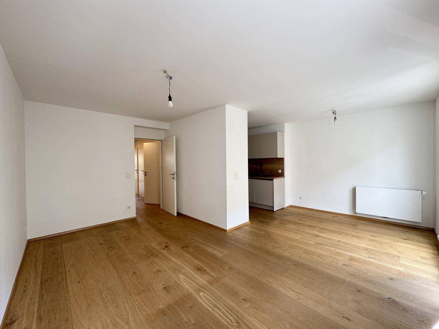 Geräumiger Wohnbereich mit Holzboden und Zugang zu weiteren Zimmern durch offene Türen.