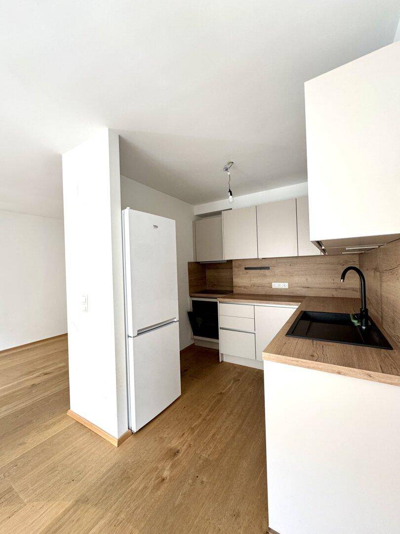 Funktionale Küche mit hellen Schränken, Holzarbeitsplatte, schwarzem Spülbecken und integriertem Kühlschrank.