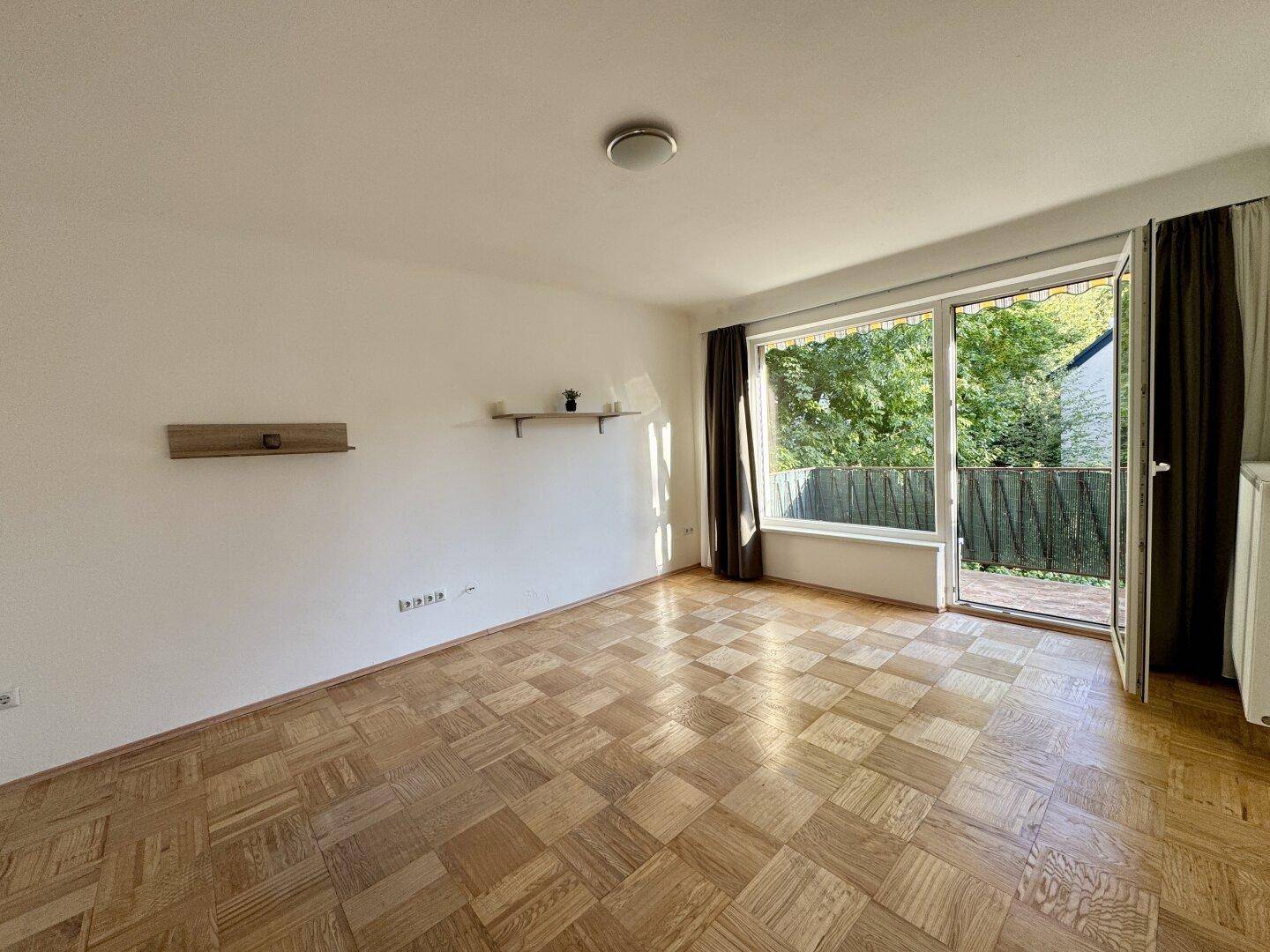 Heller Wohnraum mit Parkettboden und direktem Zugang zum Balkon, bietet viel natürliches Licht.