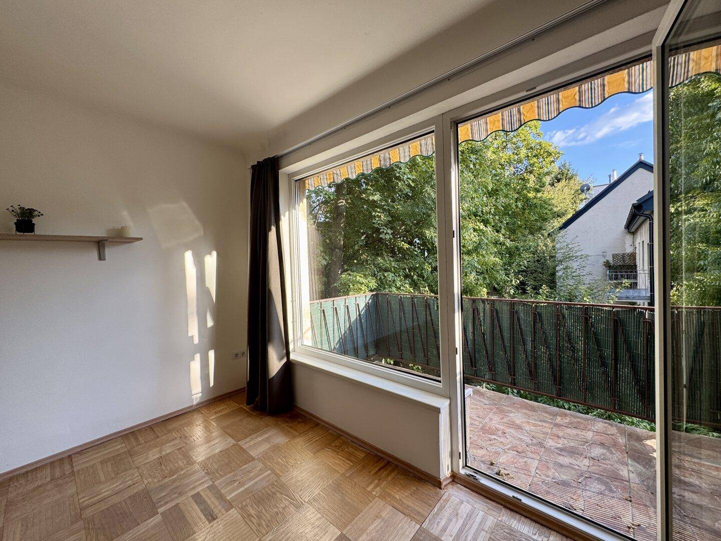 Große Fensterfront im Wohnzimmer mit Blick ins Grüne und Zugang zum sonnigen Balkon.