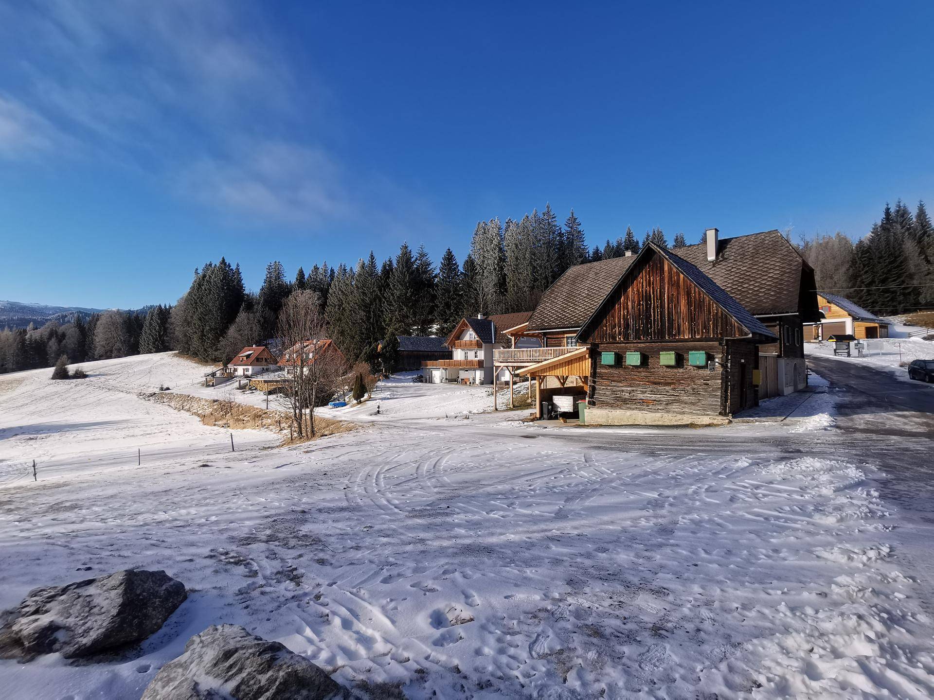 Traditionelle Holzhäuser in einer verschneiten Winterlandschaft mit weiten Feldern und Wäldern.