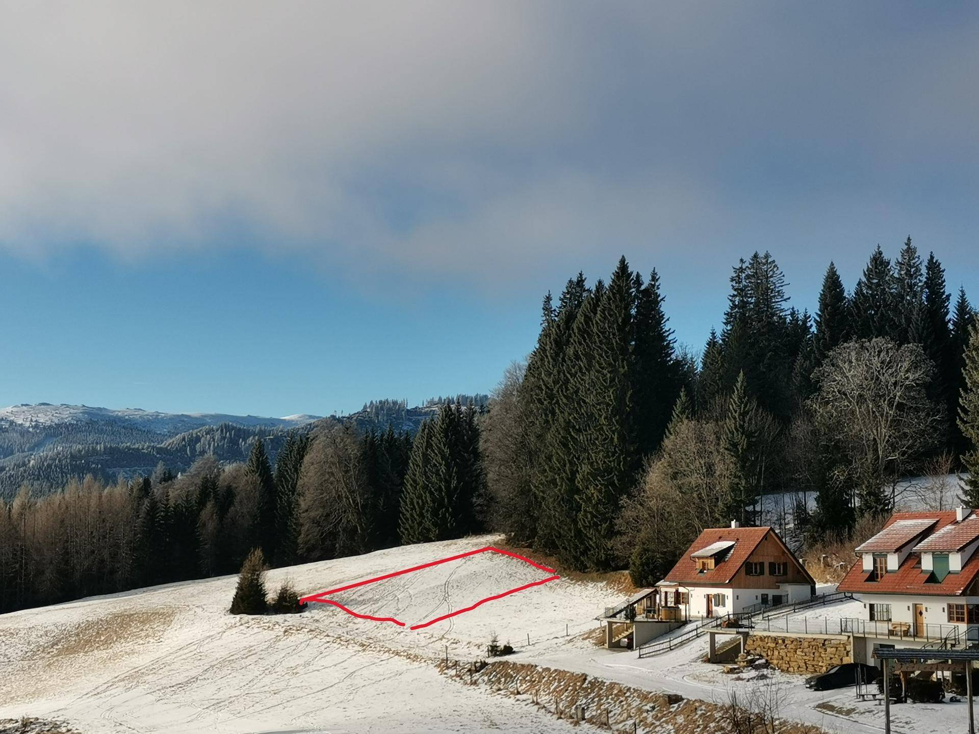 Winterliche Luftaufnahme einer verschneiten Landschaft mit Häusern und einem rot markierten Grundstück.