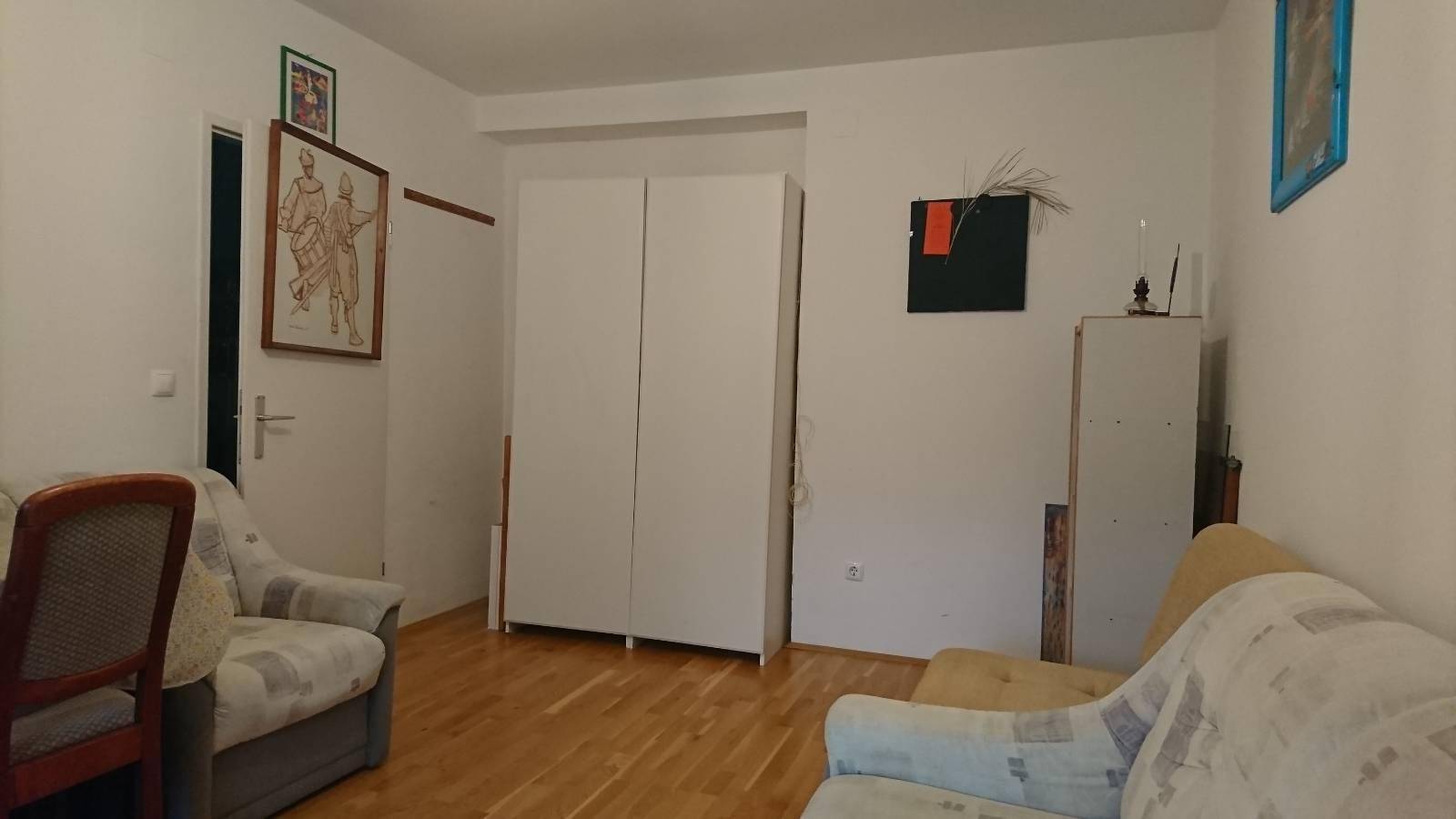 Wohnzimmer mit Holzfußboden, einem großen weißen Schrank und verschiedenen Möbelstücken.